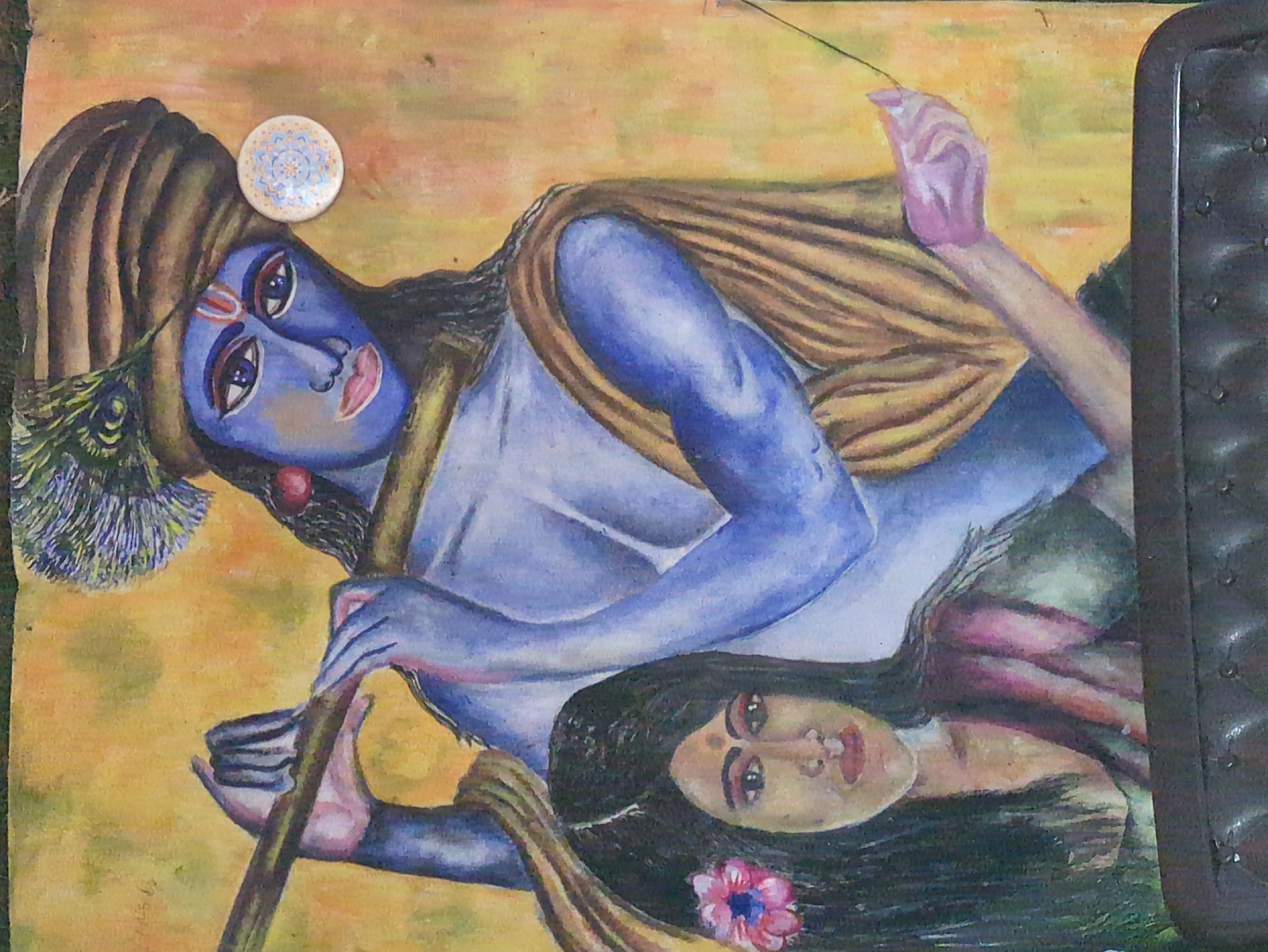 This is a painting of two figures, likely depicting a scene from Indian mythology. A male figure, with blue skin and wearing a turban adorned with a peacock feather, plays a flute. A female figure, with dark hair decorated with a pink flower, looks towards the viewer. They are set against a yellow and orange background, possibly representing a natural environment. The painting is likely located in Bhagsu, India, a place known for its spiritual significance and artistic heritage.