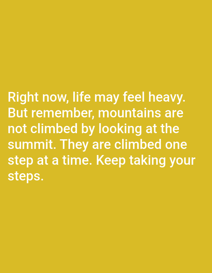 The image is a close-up shot of white text on a yellow background. The text reads: "Right now, life may feel heavy. But remember, mountains are not climbed by looking at the summit. They are climbed one step at a time. Keep taking your steps." There are no people, objects, or environmental features visible in the image. The location in the city of Алмалыбақ, Kazakhstan, is irrelevant to the content of the image.