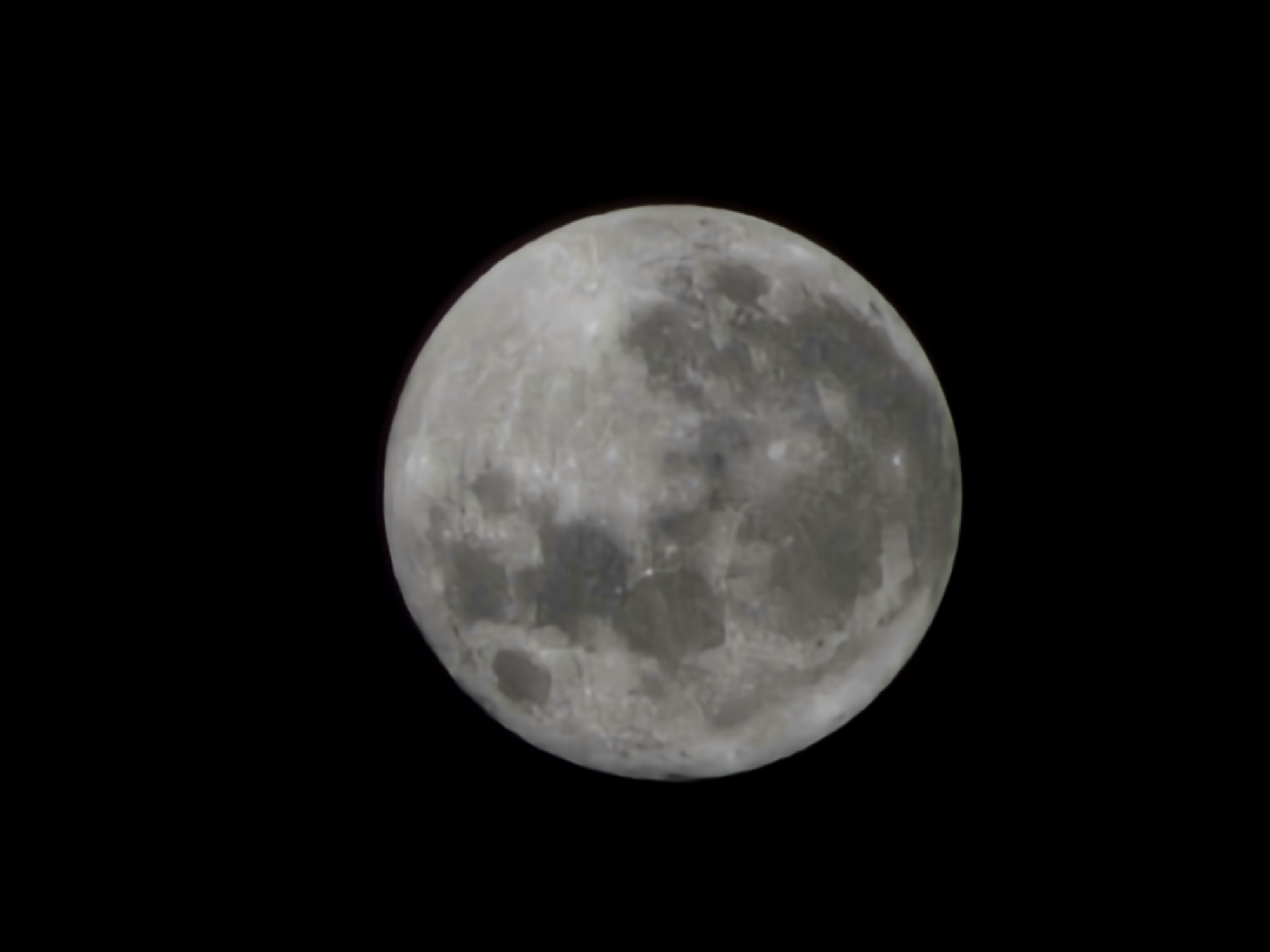 A photograph shows the moon against a black background. The moon appears nearly full, with varying shades of gray across its surface, indicative of craters and lunar maria. The image lacks any other celestial bodies or atmospheric detail. The location in Armação dos Búzios, Brazil, is not evident within the visual content of the image.