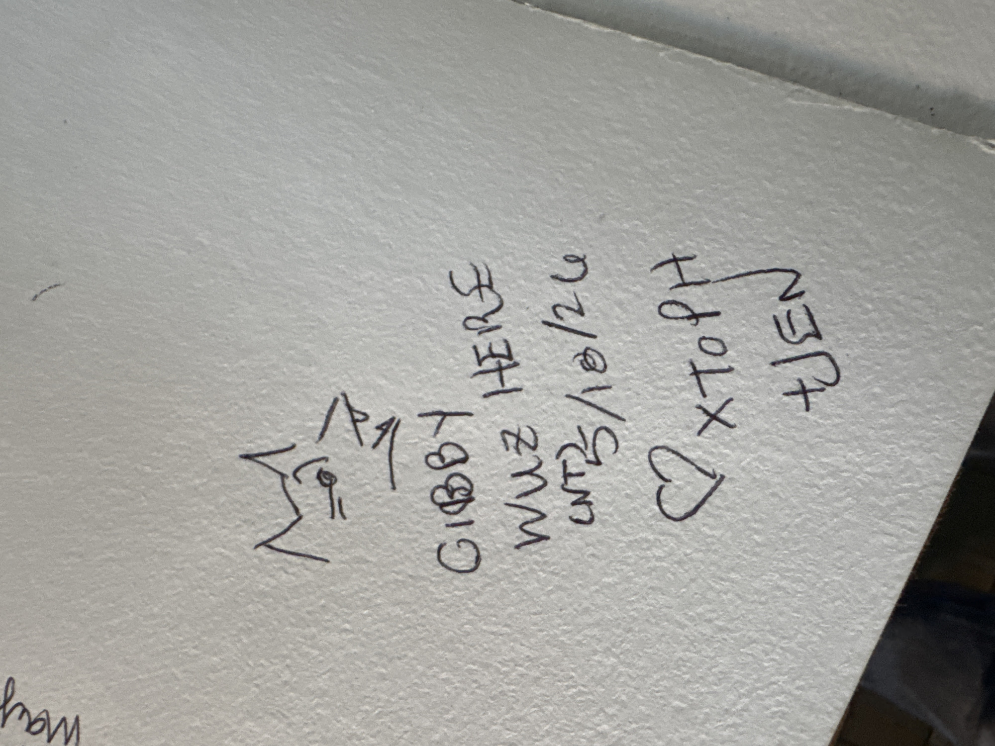 The image shows graffiti on a light-colored surface. The graffiti includes a simple drawing of a head, the text "GIBBY HERE", "WUZ NT3/18/24", a heart shape, "XtoPH", and "JEN". The location is not discernible from the image.