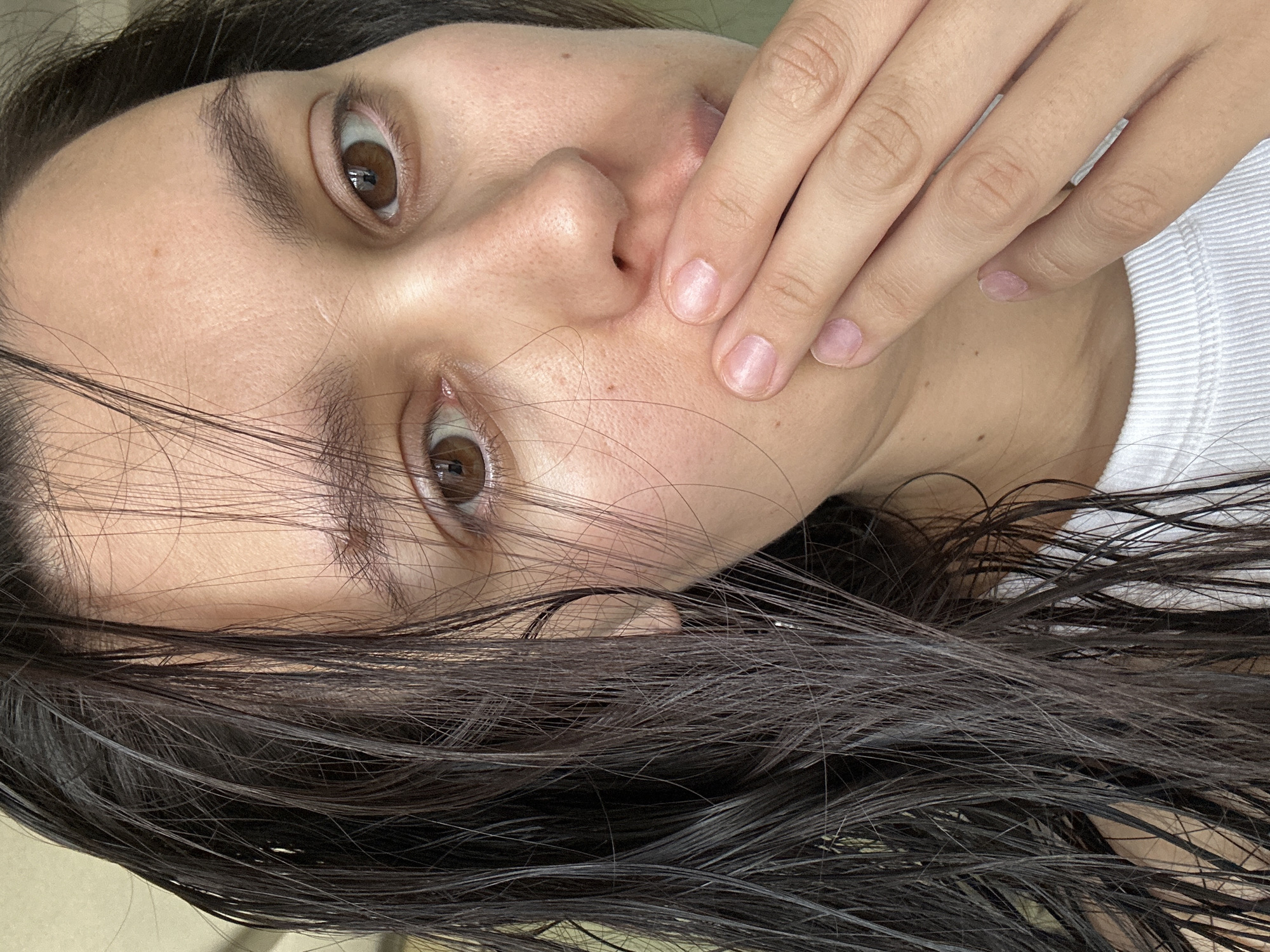 A close-up, tilted shot features a person's face, hair, and hand. The person has brown eyes, and dark, wet hair is visible in the foreground. The person's hand is raised near their mouth. The background is indistinct but may include a white shirt. No details visible suggest a specific location, such as the city of Chaikovsky, Russia.