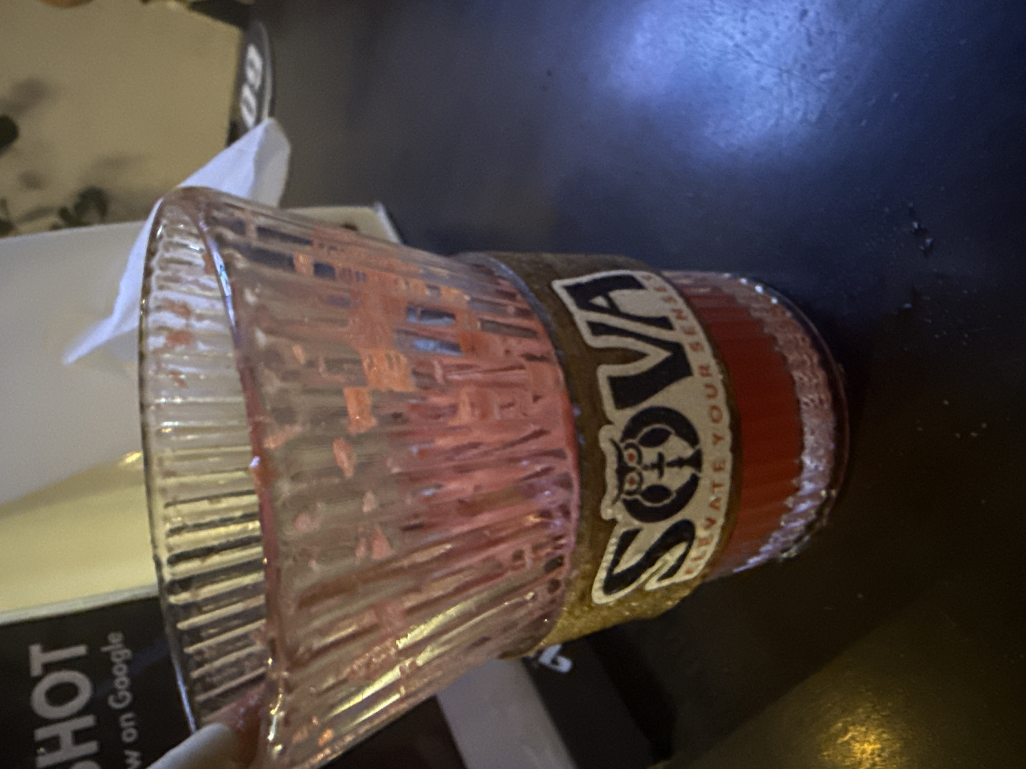 A glass cup with ridges and a label that reads "SOVA ELEVATE YOUR SENSES" sits on a dark surface. The cup appears to contain a reddish liquid. The location, city of Đà Nẵng, Vietnam, cannot be determined from the image alone.