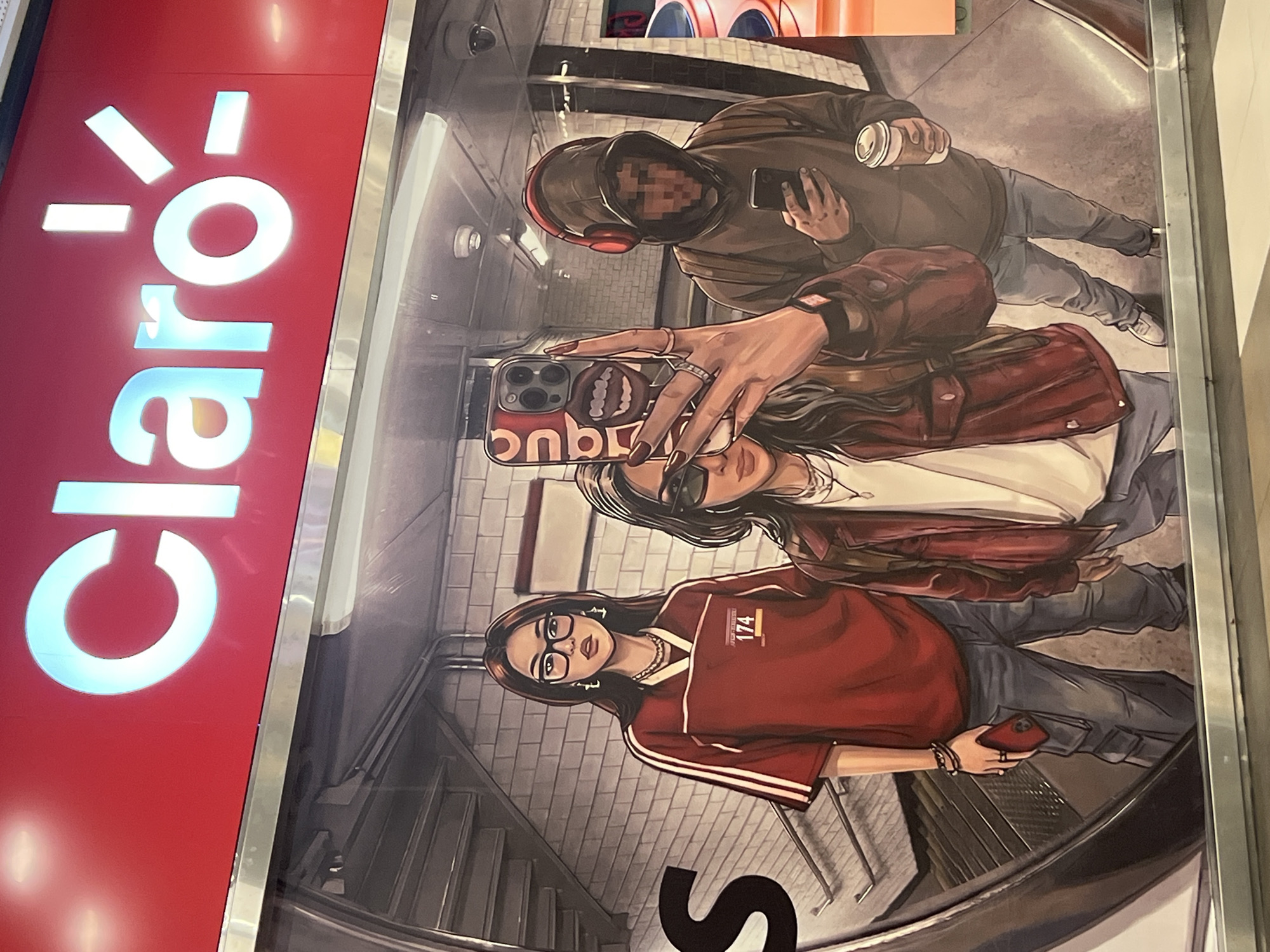 A vertically oriented image shows an advertisement for Claro, likely located in Buenos Aires, Argentina, given the brand recognition. The advertisement features a cartoonish illustration of three individuals in a subway. The topmost figure is wearing headphones and a hooded sweatshirt, obscured by a blurred-out face. The central figure is taking a selfie with a phone that has a unique patterned case. The bottom figure is wearing glasses, a red shirt with white stripes on the sleeves, and is also holding a phone. The background depicts a tiled subway station with stairs.