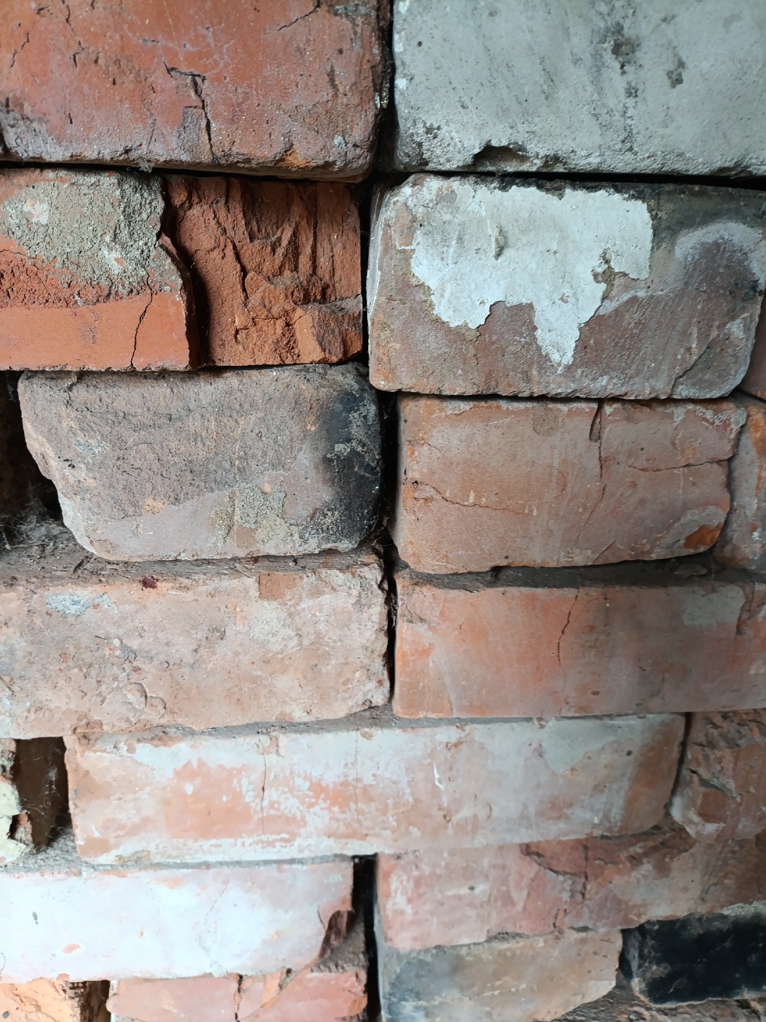 The image depicts a close-up, stacked pile of old, weathered bricks. The bricks vary in color, ranging from reddish-orange to a pale, off-white, with some showing signs of wear, chipping, and cement residue. The textures are rough and uneven. The scene appears to be an outdoor setting, possibly a construction site or storage area, given the stacked nature of the materials. There are no people or identifiable landmarks visible that would specifically link this image to Yasnaya Polyana, Russia. The lighting suggests it is daytime.