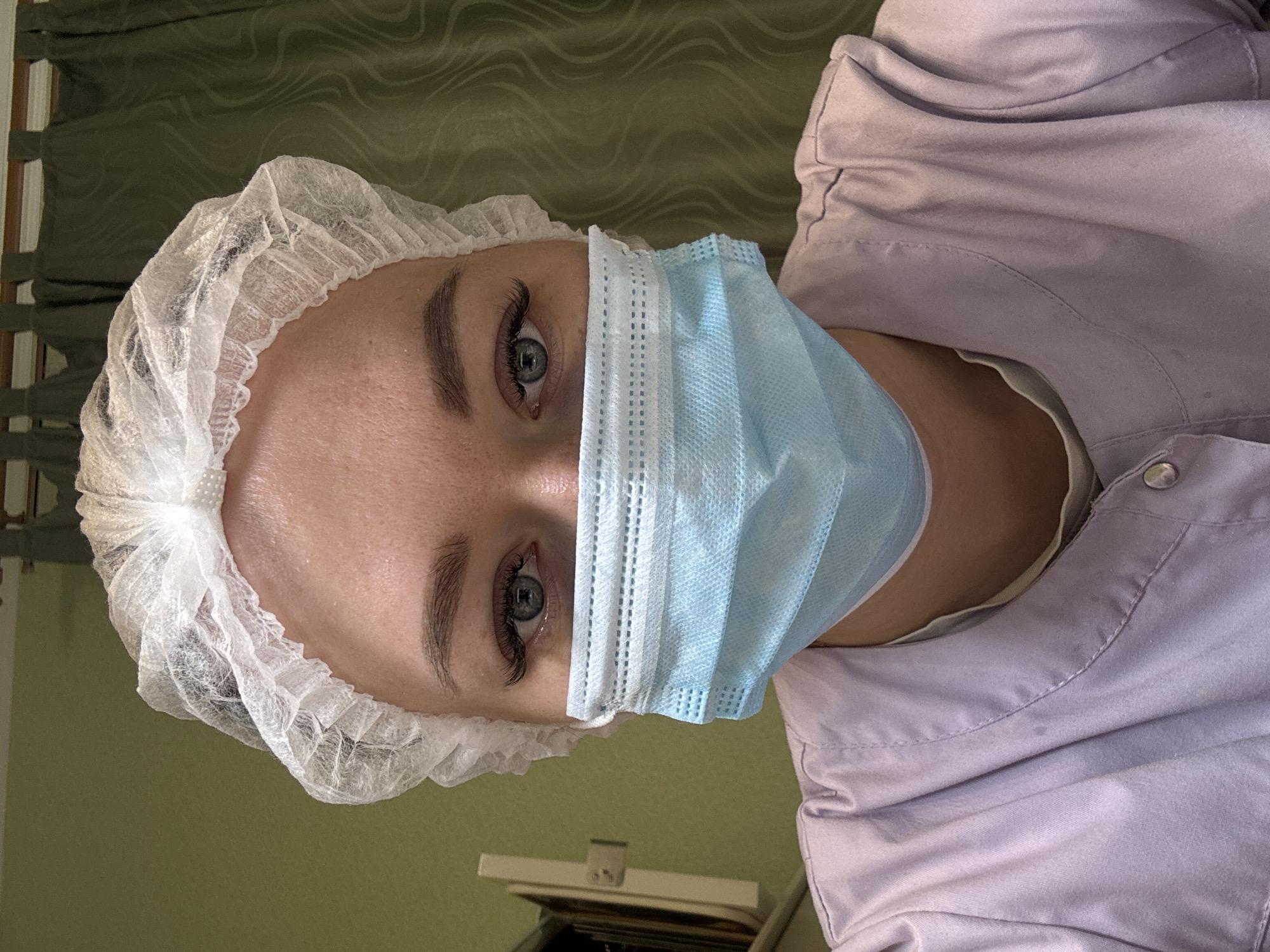 A person wearing a white surgical cap and a light blue surgical mask is visible. The person is wearing a light purple uniform shirt. The location is possibly in Ферма, Russia.