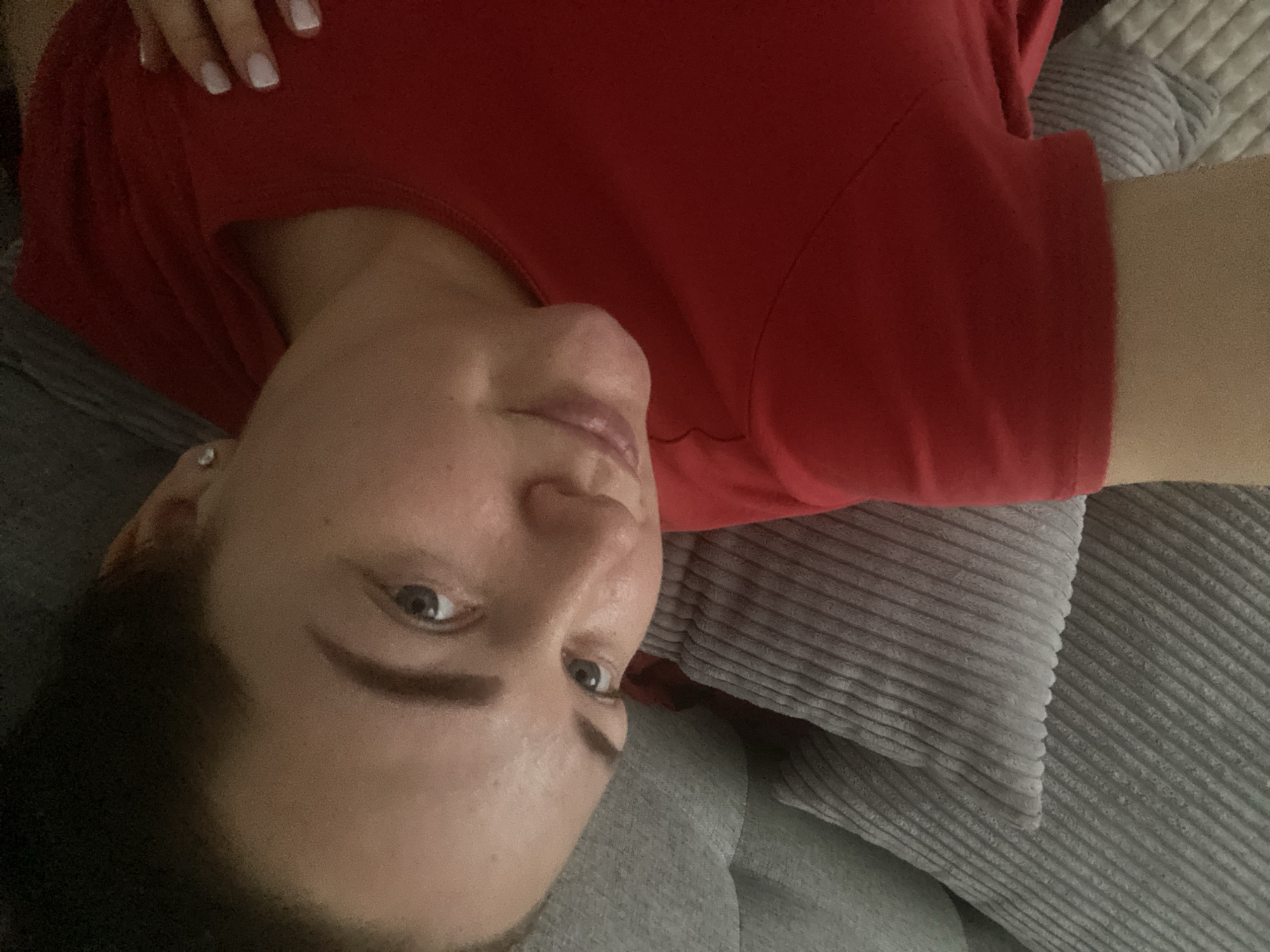 A woman is lying on a grey corduroy pillow and cushion. She is wearing a red top. Her fingernails are painted white. The setting or location within Sochi, Russia, is not discernible from the image.