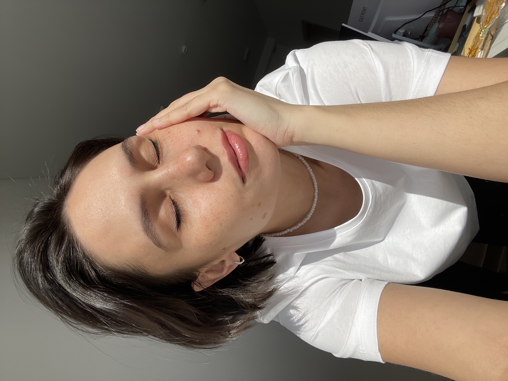 A woman is posing for a portrait. She is wearing a white t-shirt and a pearl necklace. Her eyes are closed and her hand is on her forehead. The location is not identifiable as Izhevsk, Russia, or any specific place.