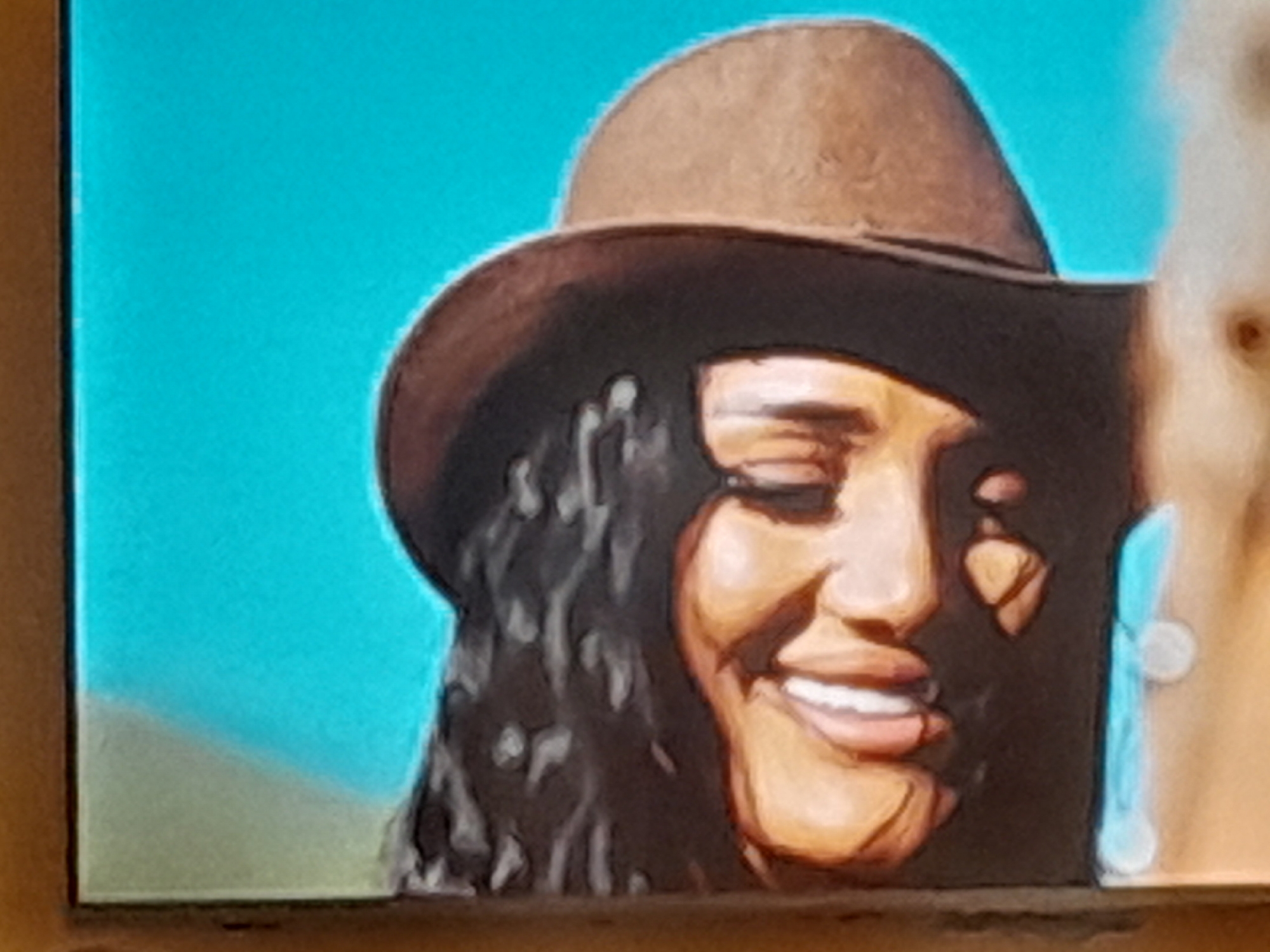 The image shows a close-up painting of a woman wearing a brown cowboy hat and dark curly hair. She has a tan complexion, dark eyes, and a wide smile showing white teeth. She is wearing a light blue earring. The background is a bright turquoise sky fading to a light green at the bottom. The image is a cropped view, and the location is unknown.