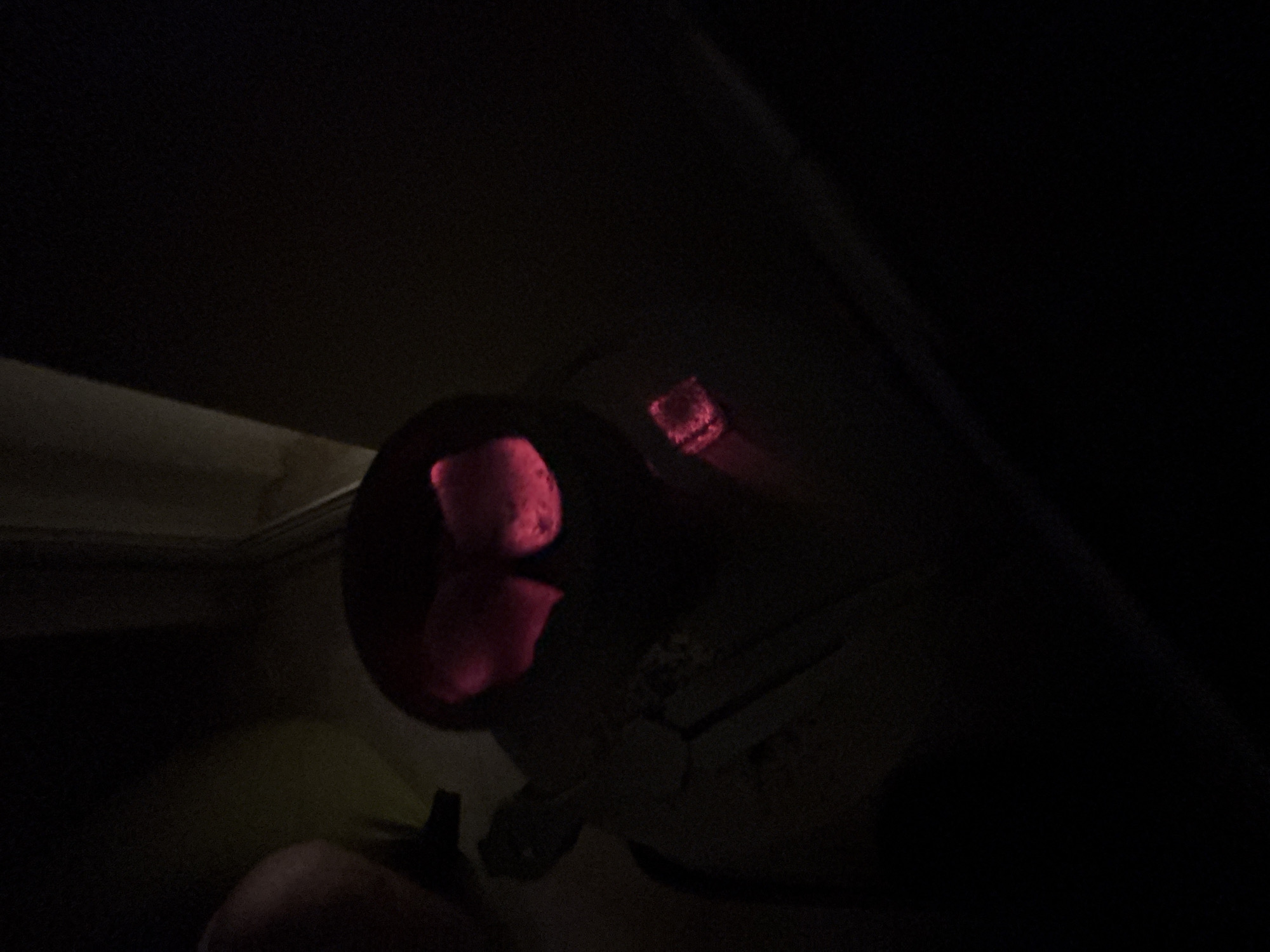The media file shows a close-up, dimly lit view of what appears to be the interior of a vehicle, possibly at night. The primary subject is a black cylindrical object, likely a car's cup holder or ash tray, containing several pieces of glowing red charcoal. The charcoal emits a vibrant pinkish-red light, illuminating the immediate surroundings within the holder. Above the cup holder, a red illuminated button or indicator light is visible, suggesting it's part of the car's dashboard or overhead console.
A hand, partially visible in the bottom left corner of the frame, is illuminated by the red glow of the charcoal, indicating someone is holding or interacting with the object. The overall lighting is very low, with deep shadows dominating the scene, characteristic of a dark environment such as nighttime or a poorly lit interior. The background is indistinct and dark, with some faint outlines of what could be the car's interior.
The glowing charcoal suggests an activity involving heat or a burning substance, possibly related to smoking or a specific type of automotive accessory. The location context of Krasnodar, Russia, does not provide specific visual cues within the image itself, but the interior setting is consistent with a vehicle. No visible text is present in the media file. The mood is somewhat mysterious due to the darkness and the unusual glowing elements.