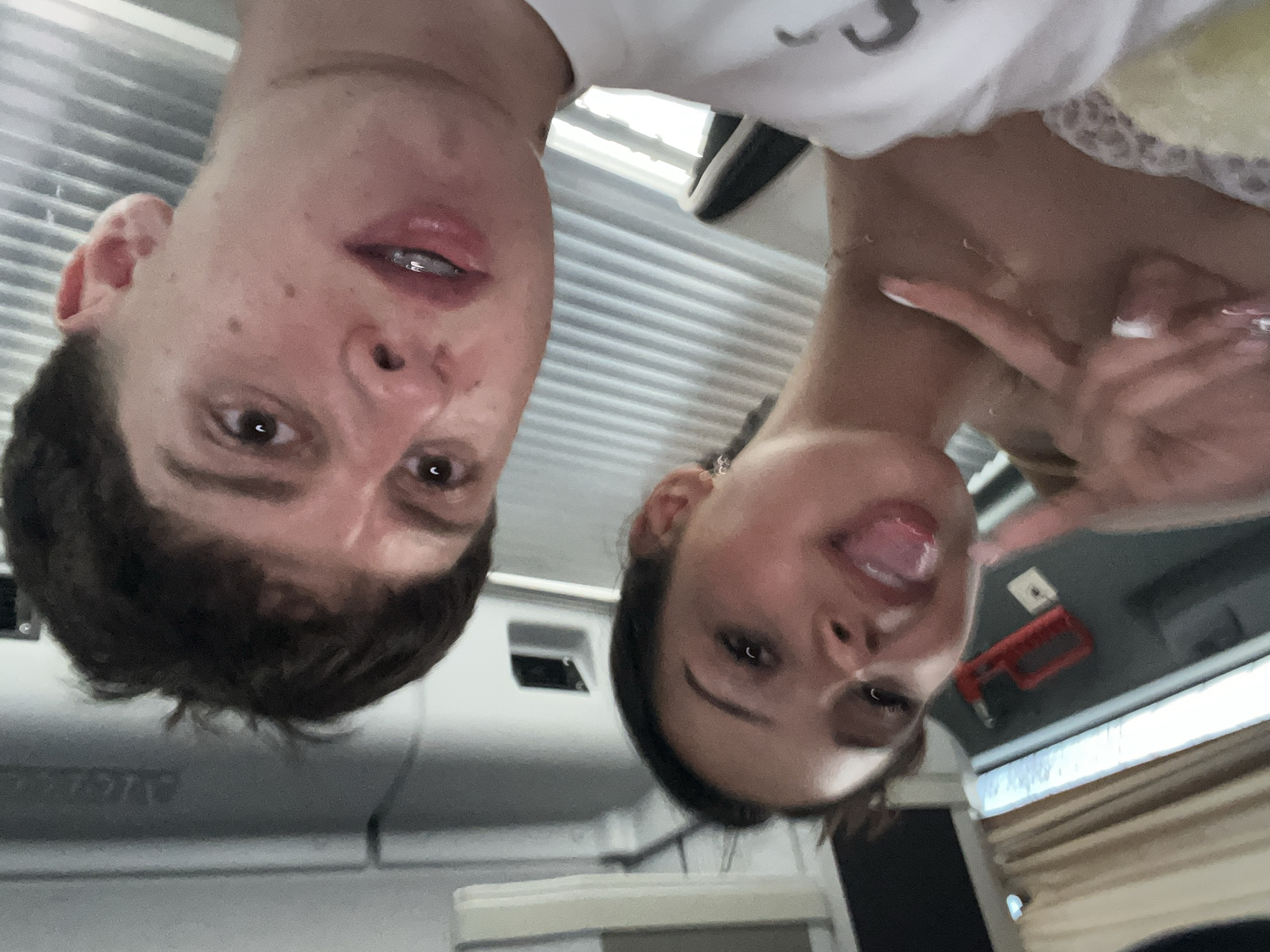 Two people, a male and a female, are posing for a photo. The male, on the left, has short brown hair and light skin. The female, on the right, has long dark hair and is sticking her tongue out while making a peace sign with her fingers. The photo is taken from a low angle, looking up at the subjects. The background shows interior elements, including what appears to be a ceiling with ventilation slats and a red emergency pull handle. There is no specific indication within the image itself that the location is Jesolo, Italy.