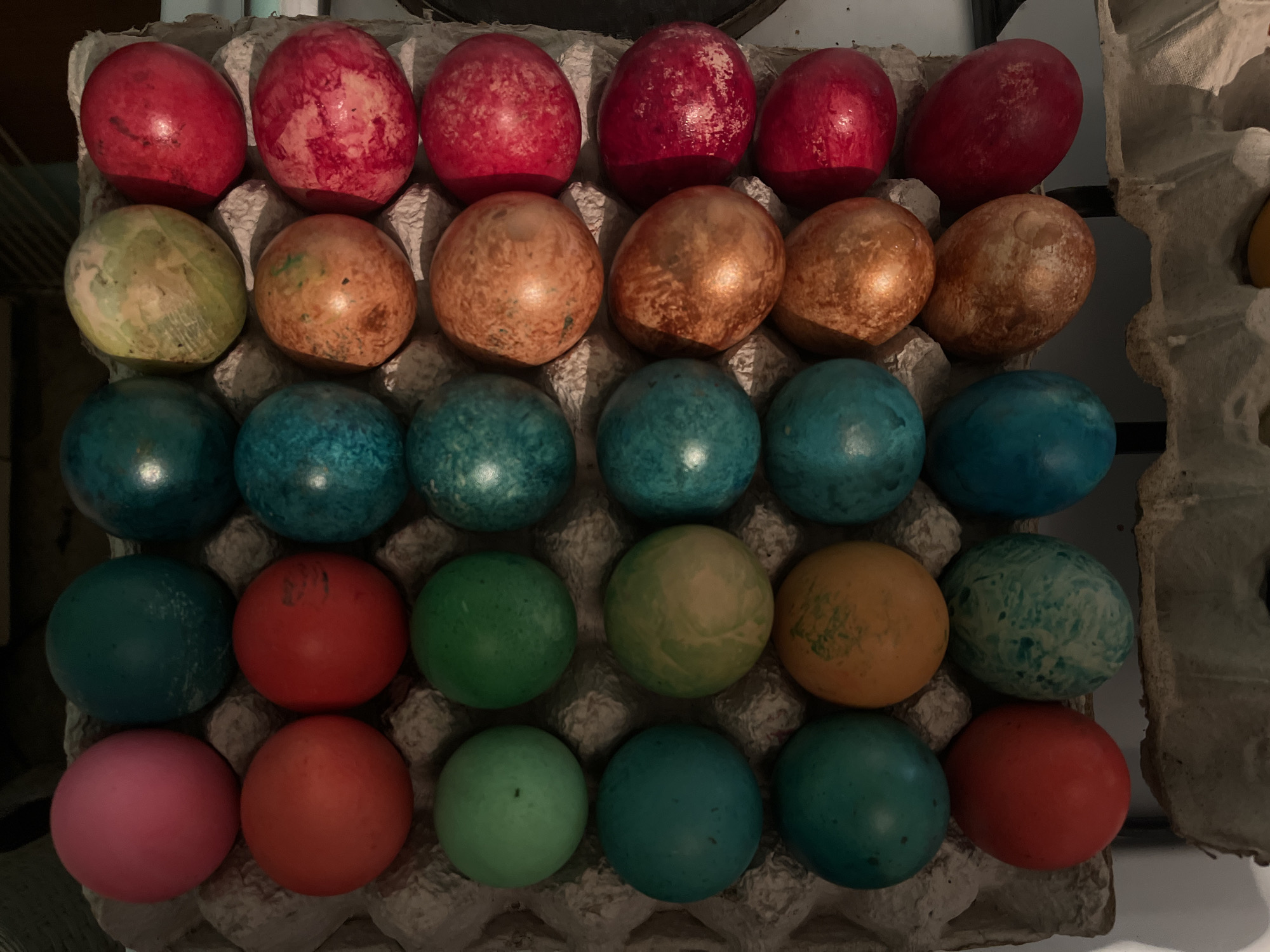 The image shows a carton of 24 colored eggs. The colors include red, orange, blue, green, and pink. The eggs are arranged in a 4x6 grid. The carton appears to be cardboard. The photograph was taken indoors. The exact location in Lozarevo, Bulgaria is not clear from the image.