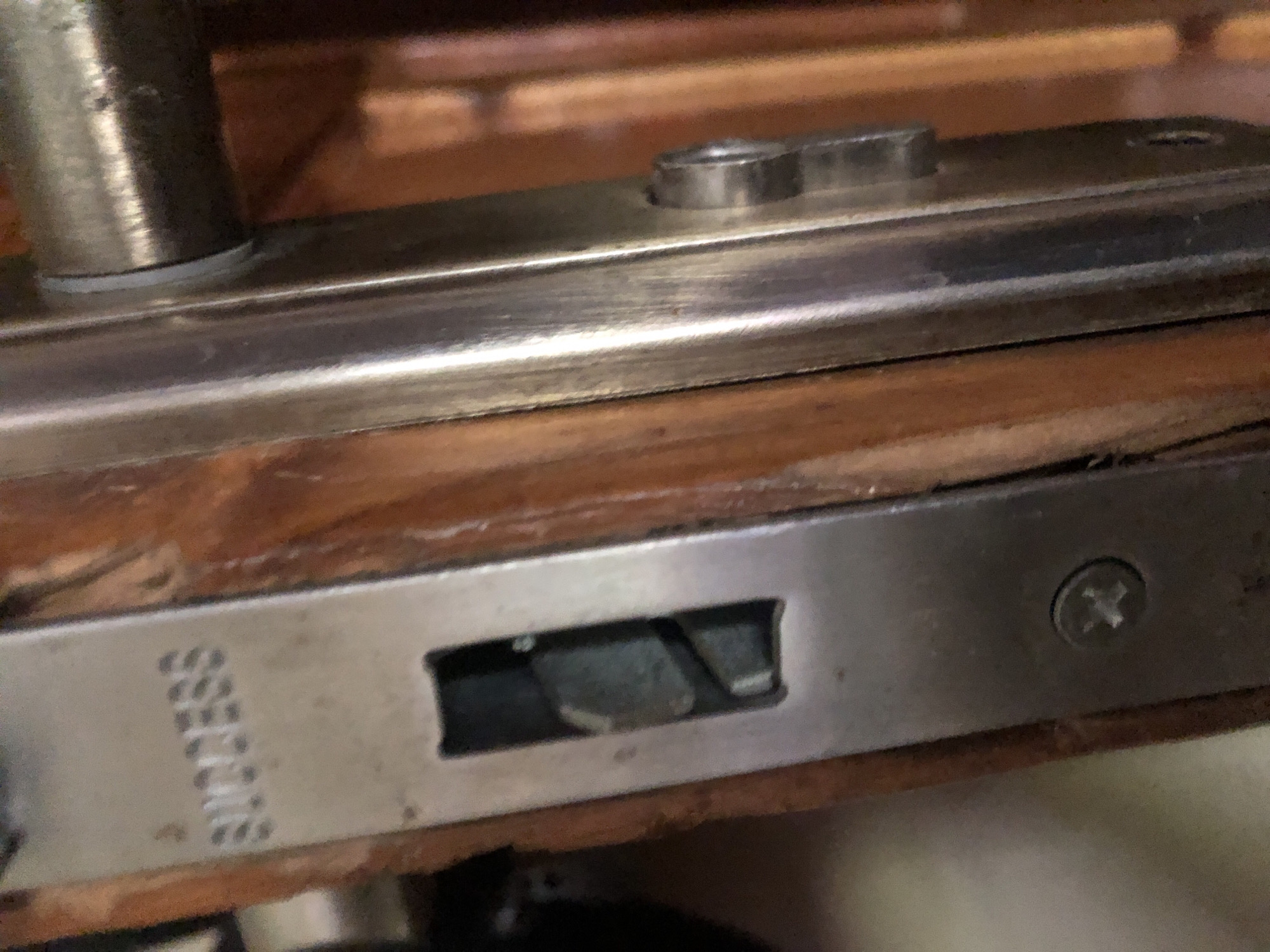 The image is a close-up shot of a door lock mechanism. The lock faceplate, made of metal, is visible against a wooden door frame. Embossed on the faceplate is the word "SUCCESS". A rectangular latch opening is present, with a metal latch visible inside. A screw is also visible in the lower part of the faceplate. To the right, parts of a door handle and its mounting are seen. The overall impression is of a functional but aged lock.