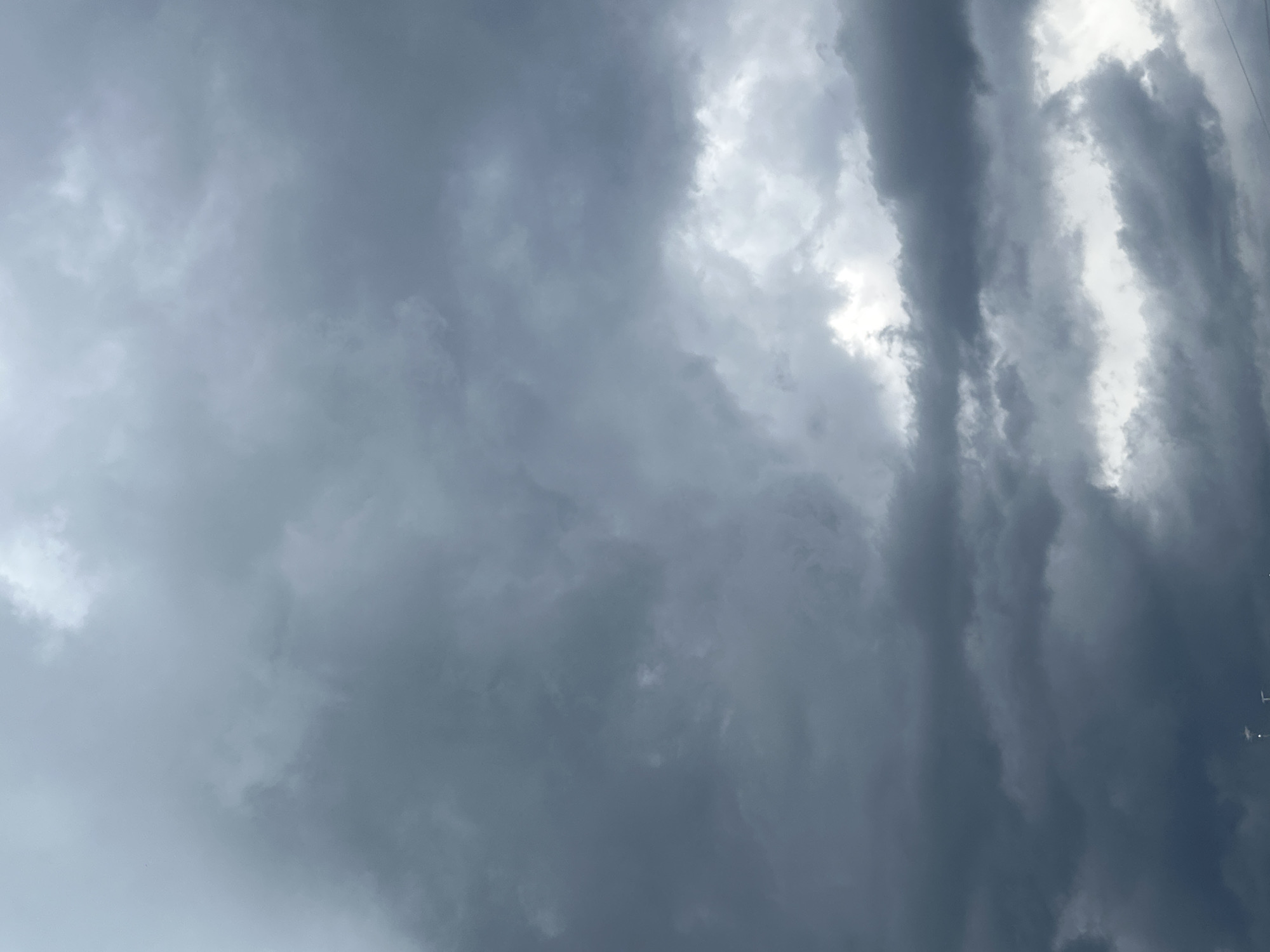 This media file depicts a dramatic sky filled with dark, turbulent storm clouds. The clouds are dense and varied in texture, with some appearing wispy and others thick and heavy. Patches of brighter sky or sunlight peek through in places, creating a contrast between light and shadow. The overall impression is one of impending weather, likely rain or a storm. There are no people or specific objects visible, only the vast expanse of the sky. The image is likely taken during daylight hours, but the heavy cloud cover suggests an overcast or stormy day. The mood is somber and powerful, evoking a sense of nature's raw energy. There is no visible text in the image.