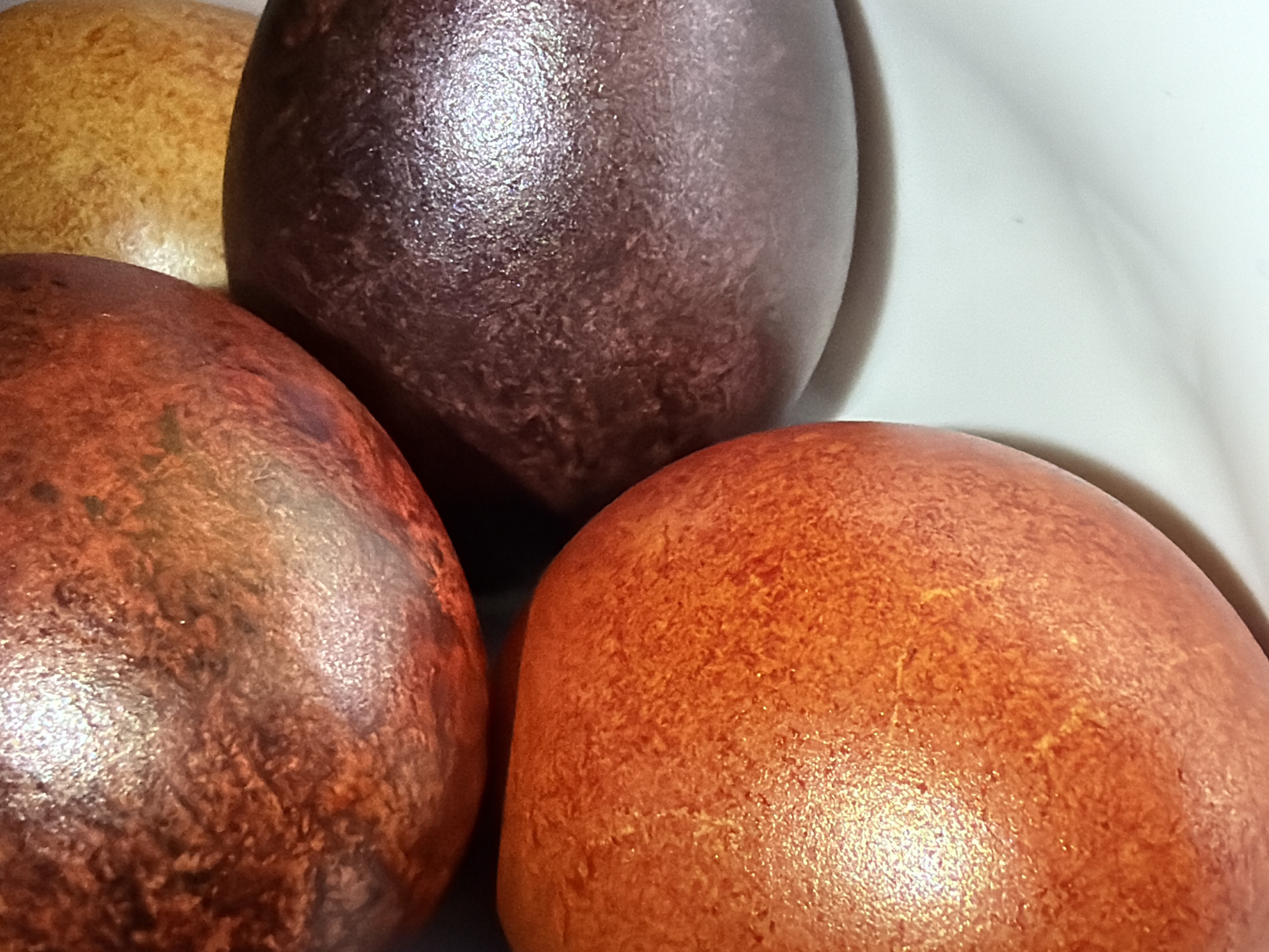 The image shows four Easter eggs in a close-up shot. The eggs are varying shades of brown, orange, and yellow, with a textured surface and slight glossiness. They appear to be resting inside a white container, possibly a bowl or a box. No people are visible. There is no information to place the image in Chaikovsky, Russia.