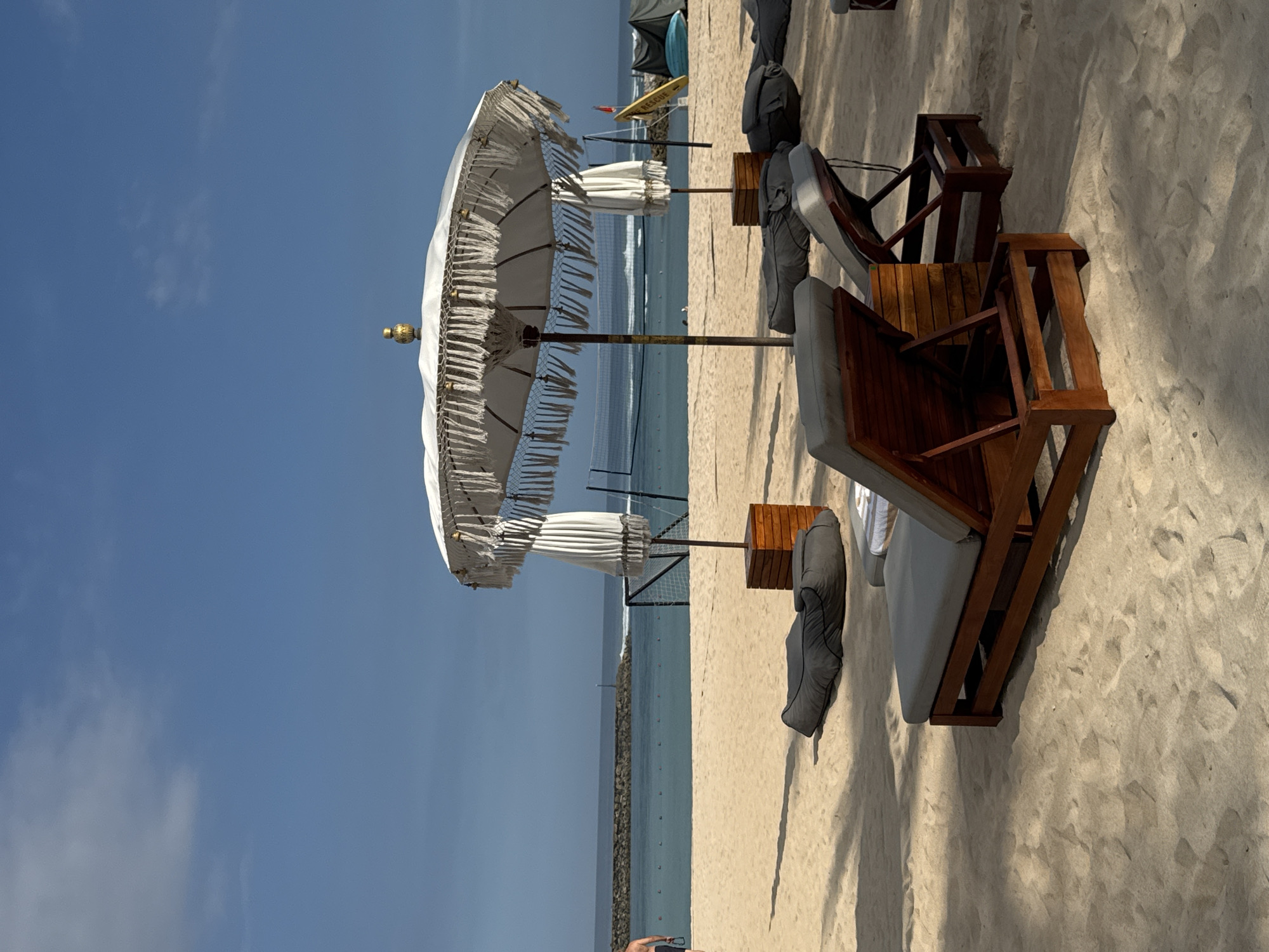 This image presents an outdoor setting at a beach. The sky is clear, indicating a sunny day. Visible are beach chairs and umbrellas which suggests it could be a resort. Based on the location of Kuta Selatan, Indonesia, it is likely a coastal area known for tourism. The objects presented are beach chairs and umbrellas. There is no mention of any person in the image.