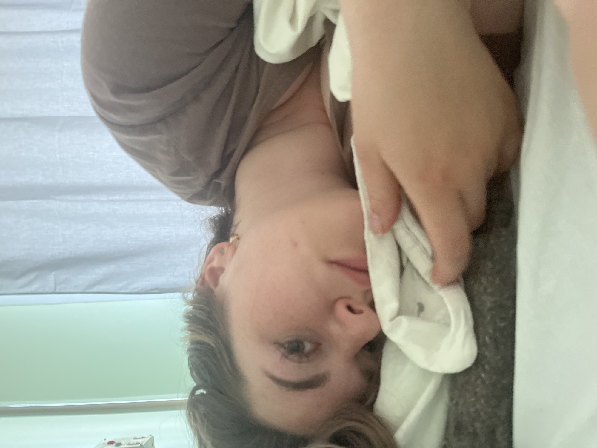 A young woman is lying in bed. She is holding a white cloth near her face. The location is impossible to determine without further information.