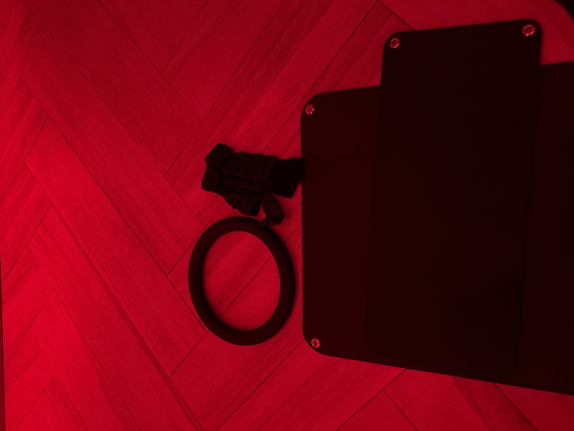 The image features a red-toned interior with herringbone wood flooring. A black round object is positioned near a darker, rectangular object attached to the flooring by metal circles. In the upper left corner of the flooring, a tangled, dark mass is visible.
Without further information, it's impossible to confirm the specific location in San Bernardino Tlaxcalancingo, Mexico. The photograph provides insufficient data to identify the exact building or setting.