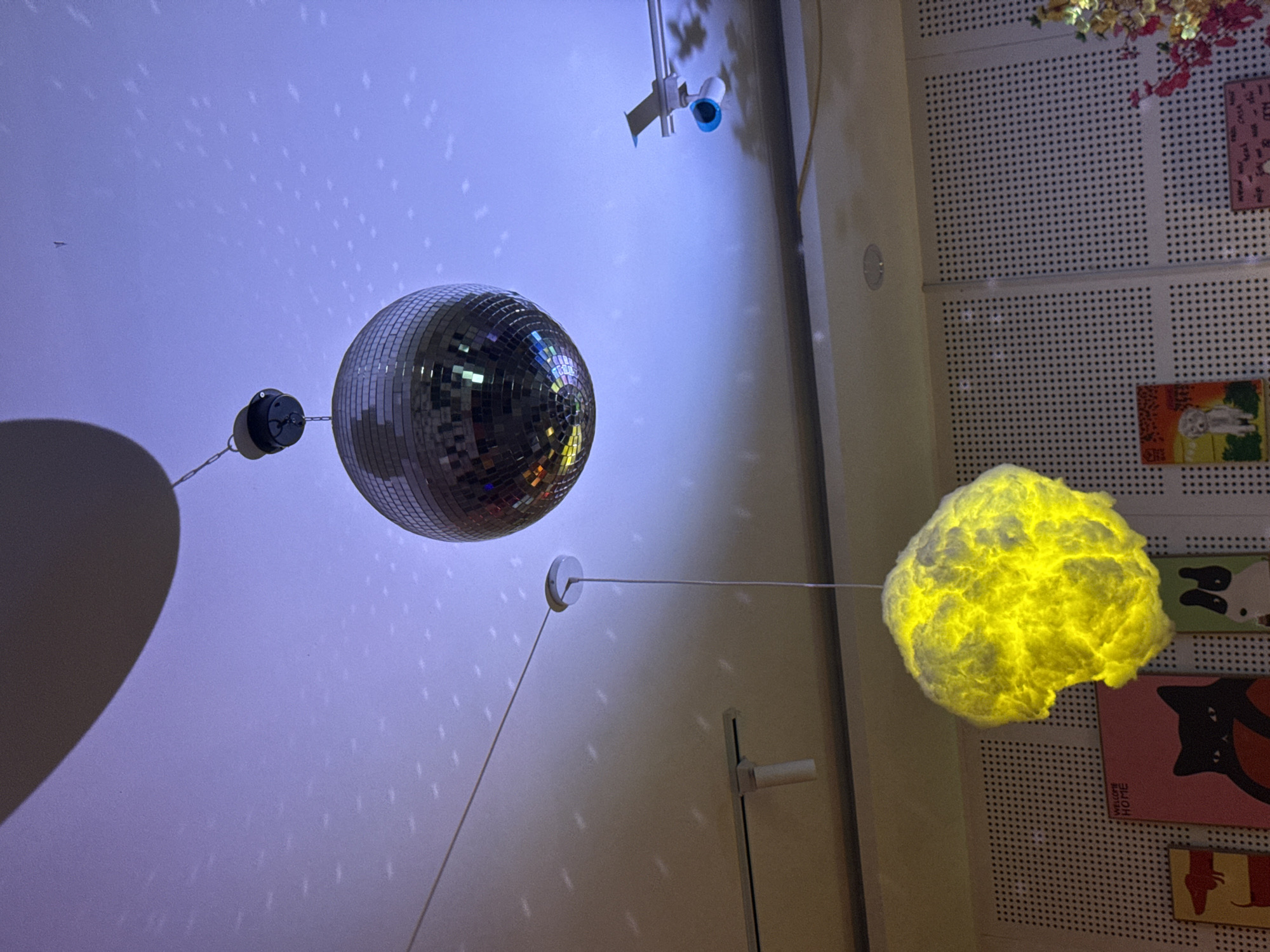 A disco ball hangs from the ceiling with a spotlight. Across the room, a yellow cloud light fixture hangs. Artwork adorns the wall. The city and country are not visible in the image, nor are any people, actions, or interactions.