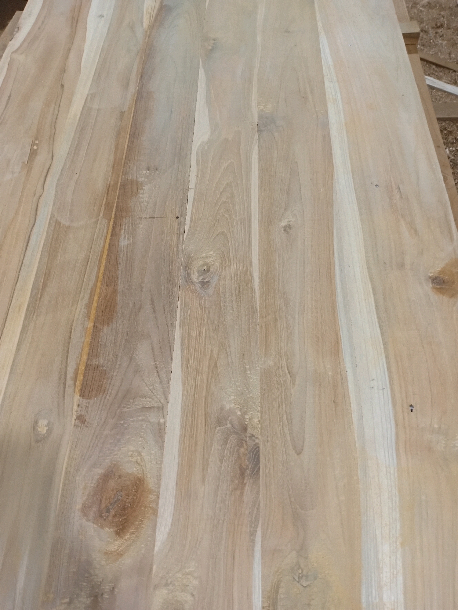 A close-up, overhead shot of a wooden surface composed of several planks. The wood has a light brown to tan color with visible grain patterns and occasional knots. The planks appear to be laid parallel to each other and extend across the frame. Some planks have slight variations in color, with some sections appearing lighter or darker than others. There are no people or other objects visible in the image. The context of Playen, Indonesia, does not appear to be depicted or implied by the visual information in the photograph.