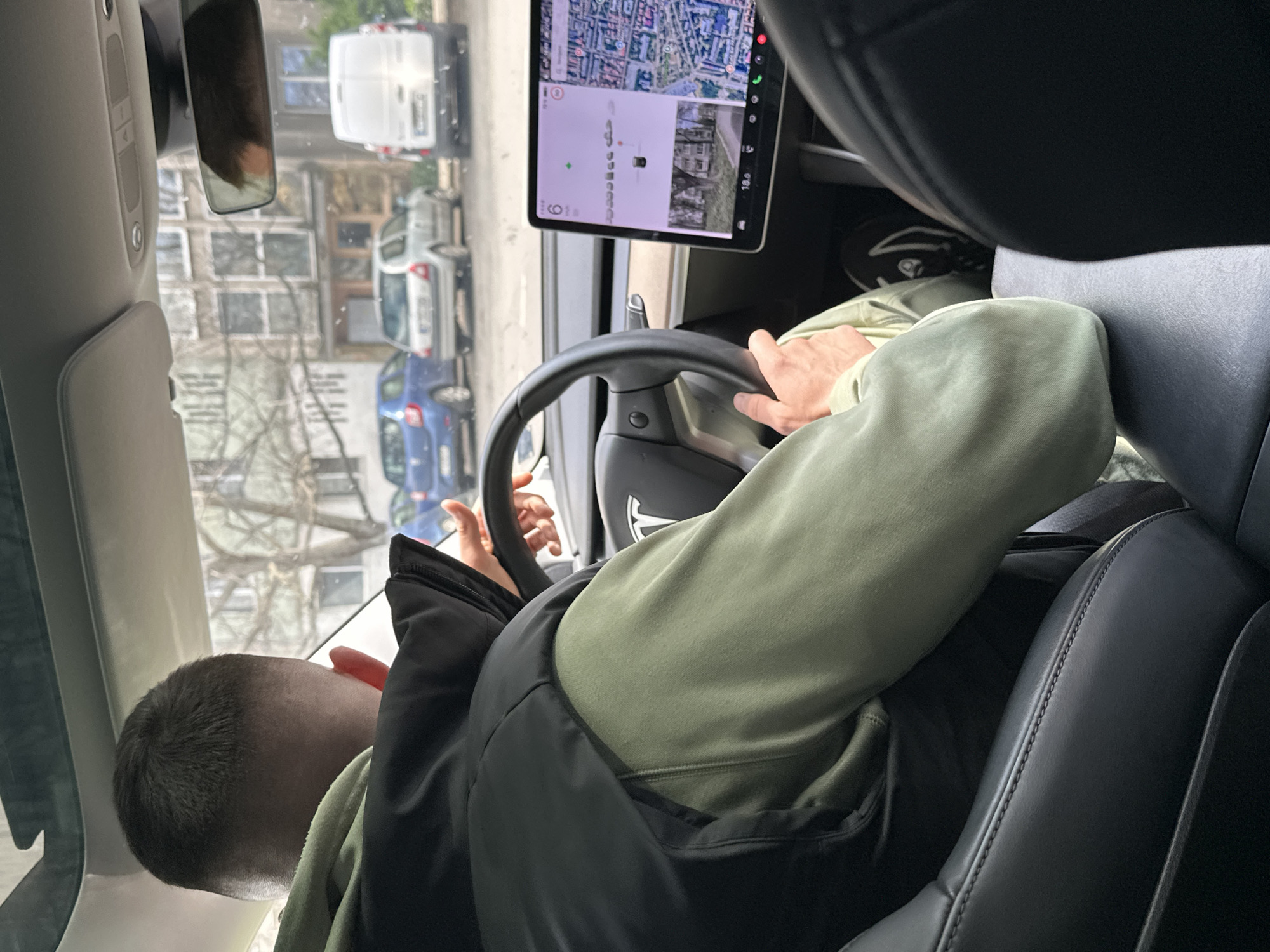 A person is driving a car in Stara Zagora, Bulgaria. The person is holding the steering wheel. The car has a navigation system displaying a map of the city. The car appears to be on a street with buildings visible in the background through the window and rearview mirror.