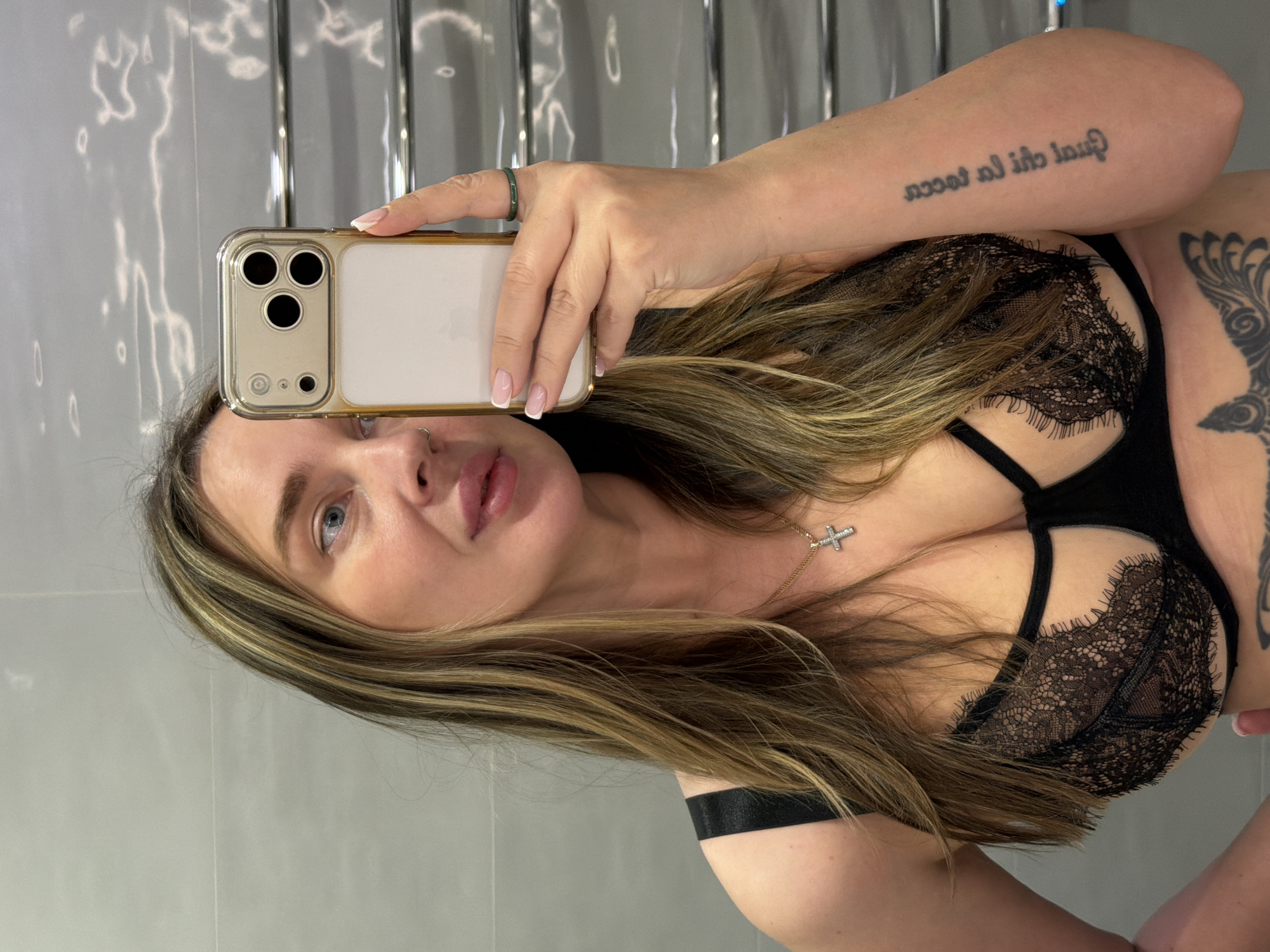 A woman is taking a selfie in what appears to be a bathroom. She is wearing a black lace bra. The background features a tiled wall and a towel rack. There is no information in the image to confirm the location in the city of Khimki, Russia.