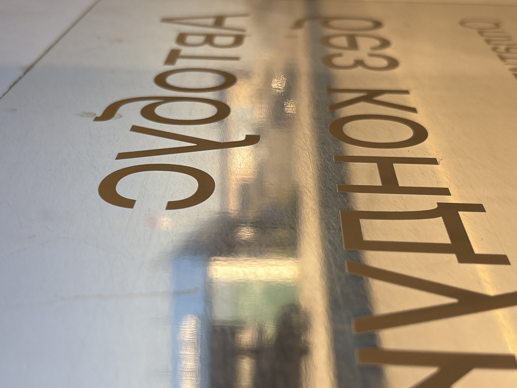 The image shows a close-up of a reflective surface with text in Cyrillic script. The text appears to read "АВТОБУС" and "КОНДУКТОР 063". The reflection suggests a busy urban environment. Based on the language and information, this image likely originates from Izhevsk, Russia. The presence of "Автобус" (Bus) and "Кондуктор" (Conductor) indicates that the image is from public transport, possibly a bus or bus stop.