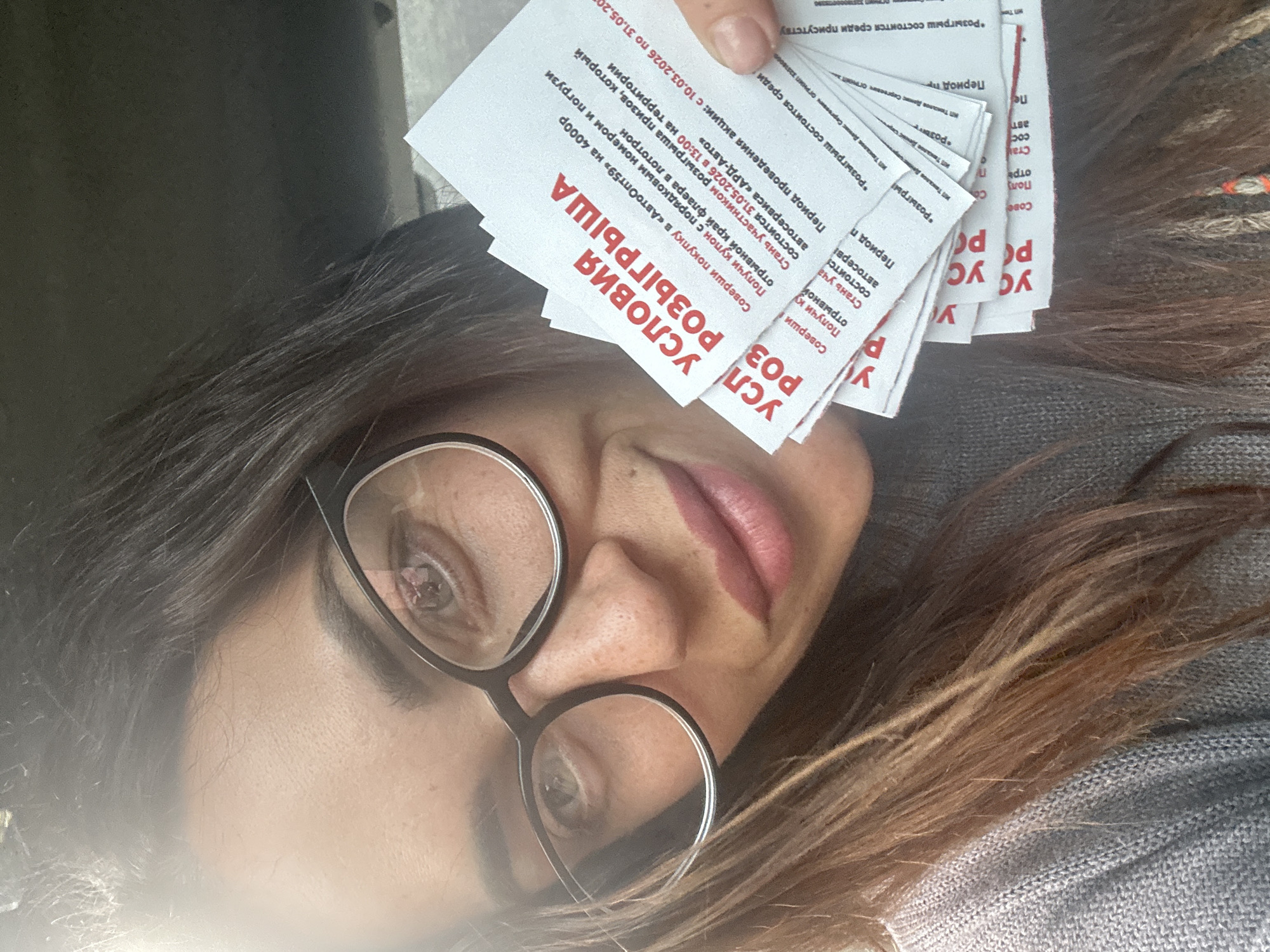 A woman with brown hair and glasses is holding several promotional flyers in her hand. The flyers advertise a prize drawing (розыгрыша) with conditions (условия) for participation. The drawing will take place on May 31, 2026 at 13:00 at the "ARD-Auto" auto service center. The promotion period is from March 10, 2026 to May 31, 2026. To participate, one must make a purchase in "AutoOpt59" for 4000 rubles, obtain a coupon with a serial number, and deposit the tear-off edge of the flyer into the lottery drum. The flyers also mention the name of individual entrepreneur Denis Sergeyevich Takalov.
The location is Chaikovsky, Russia, based on the company name AutoOpt59 operating in that city.