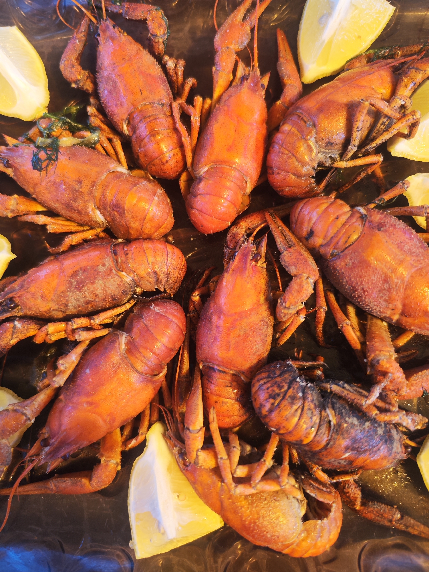 The image shows a close-up of cooked crawfish arranged on a black surface, interspersed with wedges of lemons. The crawfish are bright red, indicating they have been boiled. The exact location in Chaikovsky, Russia, is not discernible from the image.