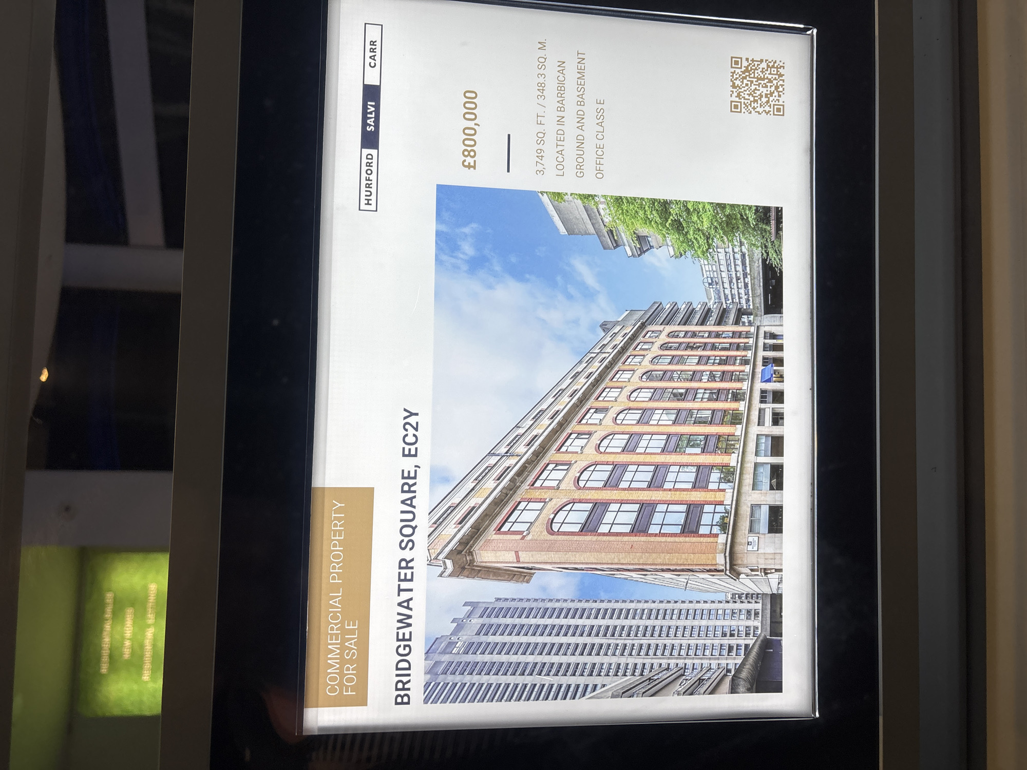 The image is a real estate advertisement for a commercial property located at Bridgewater Square, EC2Y, in the Barbican area of London, United Kingdom. The property is for sale for £800,000 and is described as 3,749 sq. ft. / 348.3 sq. m. with a ground and basement floor and is classified as Office Class E. The advertisement features a photo of the building, with the sky in the background. The real estate agency advertising the property is Hurford Salvi Carr. There is also a QR code.