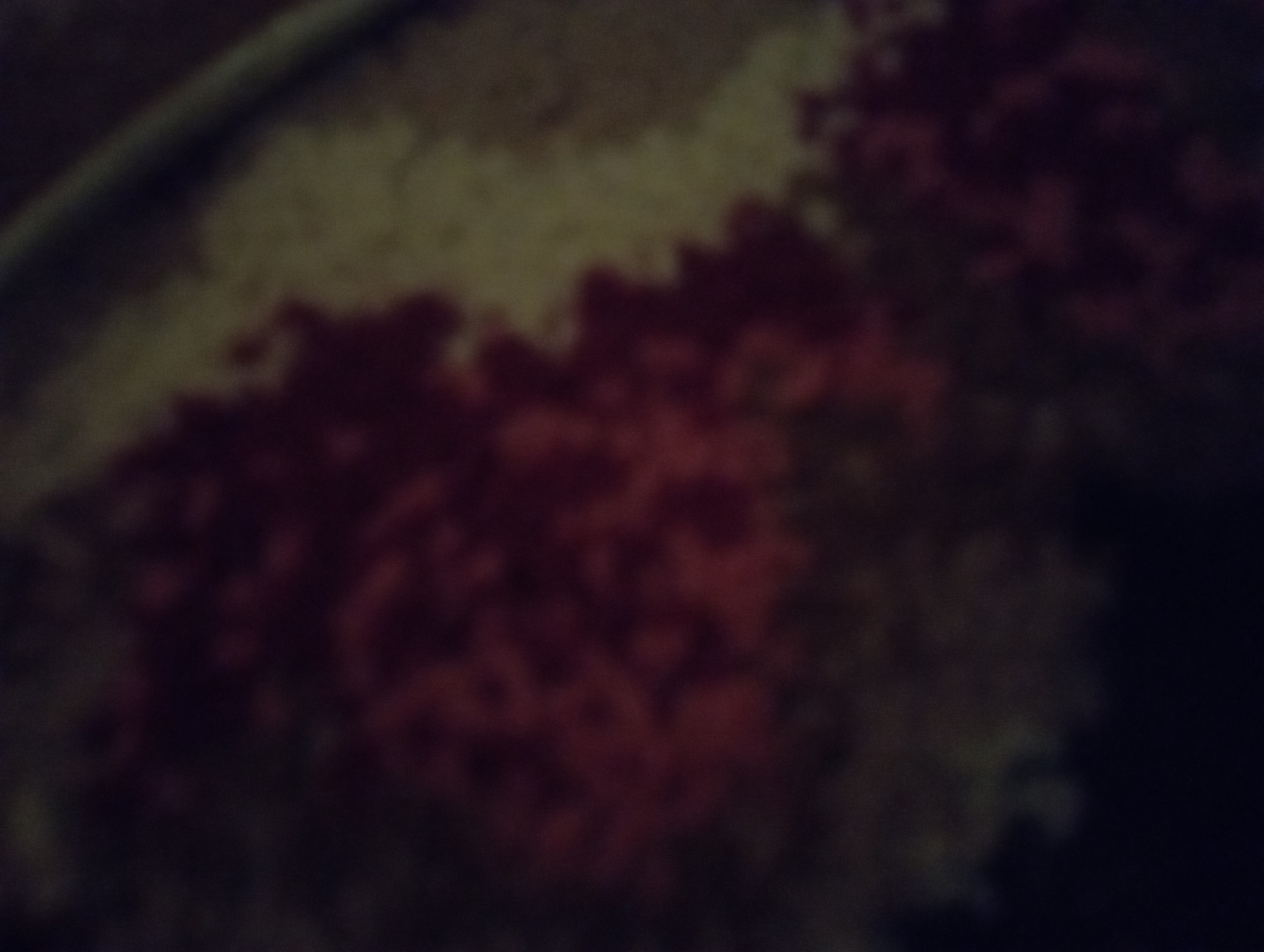 The image is a blurry, close-up view of what appears to be a patterned fabric or surface. There are distinct areas of reddish-brown and lighter tan or beige colors, arranged in a somewhat abstract or mosaic-like pattern. The lighting is dim, creating shadows and obscuring fine details. There is no discernible information about the location in Ezbet Michel Hamawi, Egypt, nor are there any people, specific objects, or actions visible in the image due to its blurriness and abstract nature.