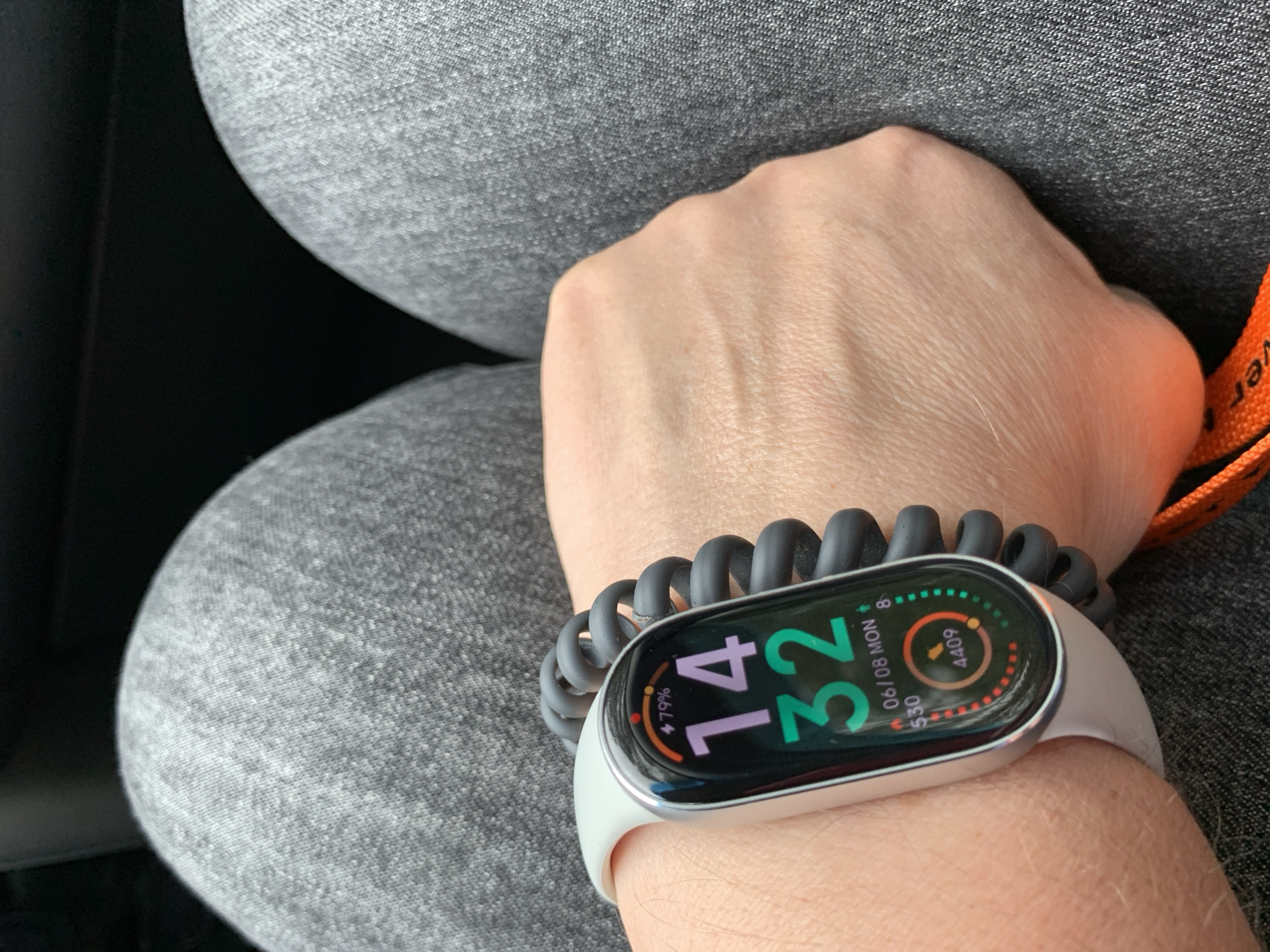 An overhead shot shows a person's left wrist wearing a smartwatch with a gray band and a coiled black strap extender. The smartwatch display shows the time as 14:32, a date of 06/08 MON, a battery level of 79%, and step count data. The wrist is resting on the person's lap, which is covered by gray jeans. The background is dark and out of focus. There are no discernible elements that would suggest a specific location within Сваткаўскі сельскі Савет, Belarus.