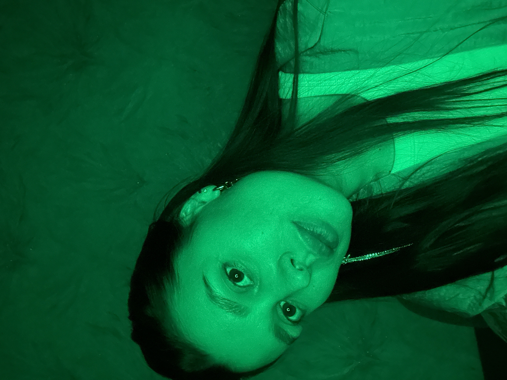 A close-up, green-toned photograph shows a woman's face with long, dark hair. She is wearing an earring. The background has a textured appearance. There is no information to suggest the photograph was taken in the city of Chaikovsky, Russia.