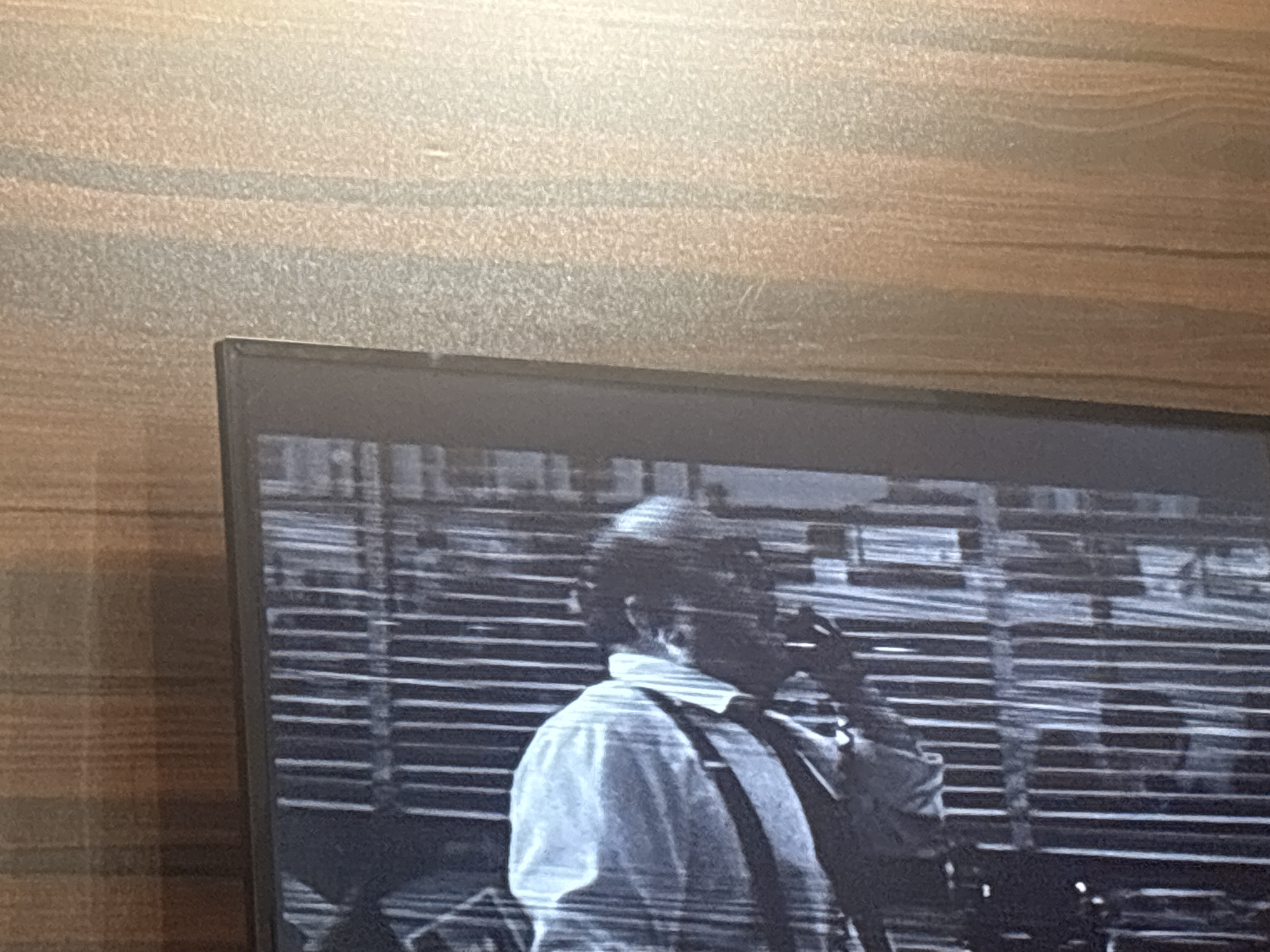 The image shows a black and white scene displayed on a television screen, partially framed by a light-colored wooden surface. In the scene, a man is visible, wearing a light-colored shirt and suspenders. He appears to be standing in front of horizontal blinds. The scene has an old-fashioned, film-like quality. The location is not discernible as Eneka, Nigeria from the available image.