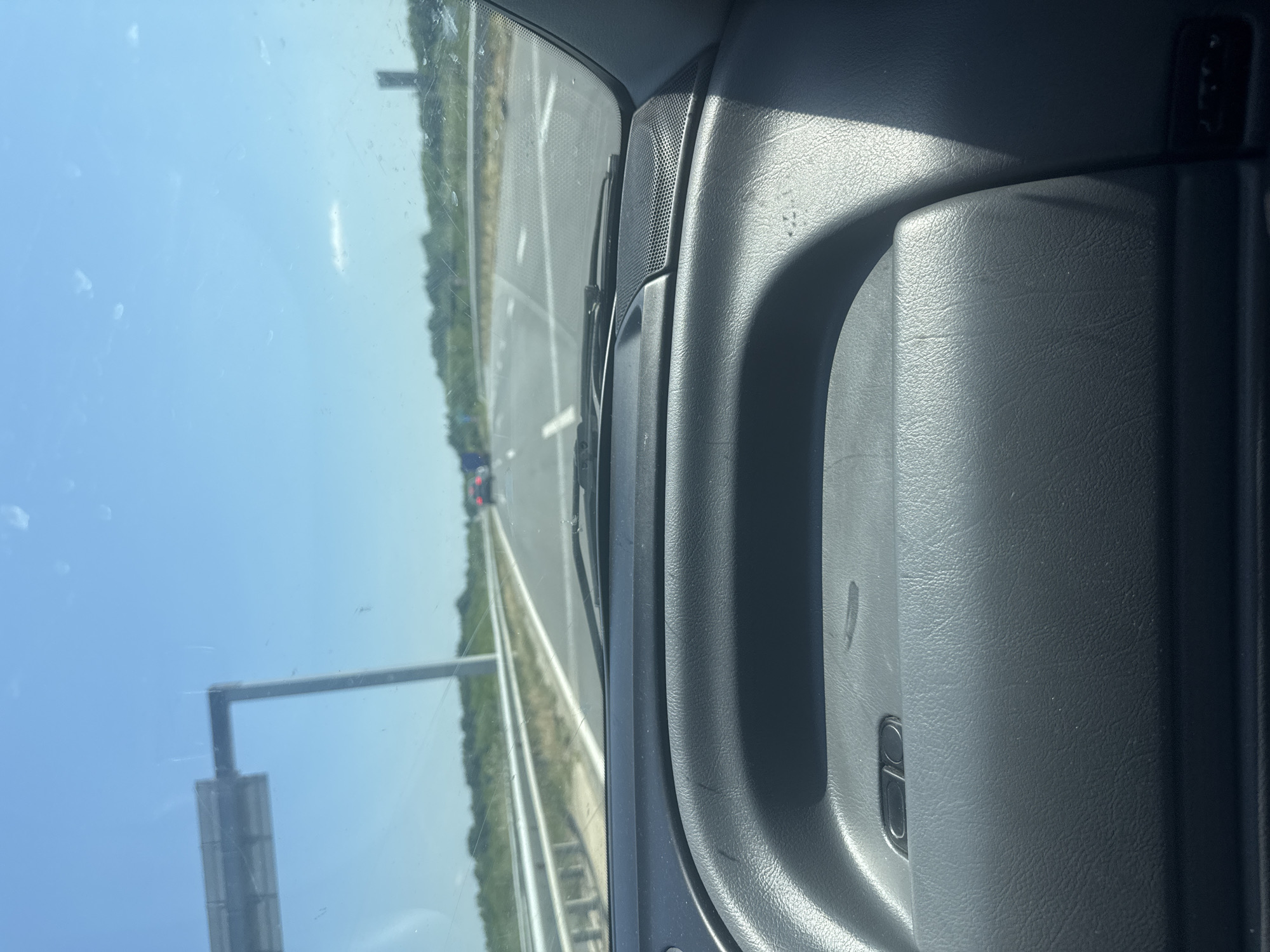 A view from inside a vehicle driving on a highway near Zagore, Bulgaria. The highway is multi-lane with a median and roadside vegetation. There are other vehicles visible in the distance. A road sign is present on the left side of the highway. The interior of the car is visible, including the dashboard and door panel.