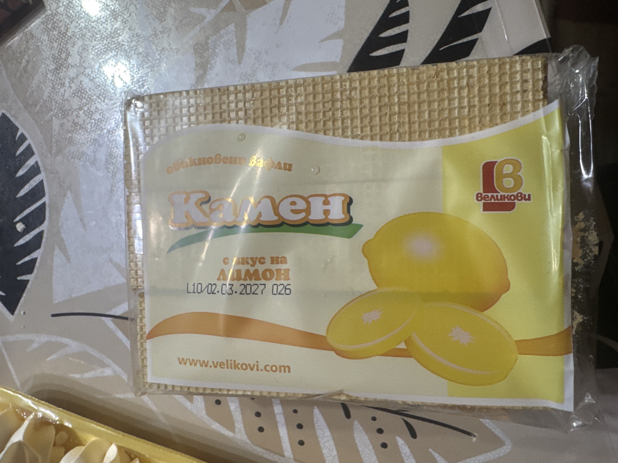 The image shows a packaged wafer labeled "Камен" ("Kamen") with lemon flavor ("с вкус на лимон"). The packaging also includes the expiration date "L10/02.03.2027" and a code "026." The brand logo "Великови" ("Velikovi") is visible, along with their website "www.velikovi.com". The product is located in Sarnevo, Bulgaria, based on the brand's locality.