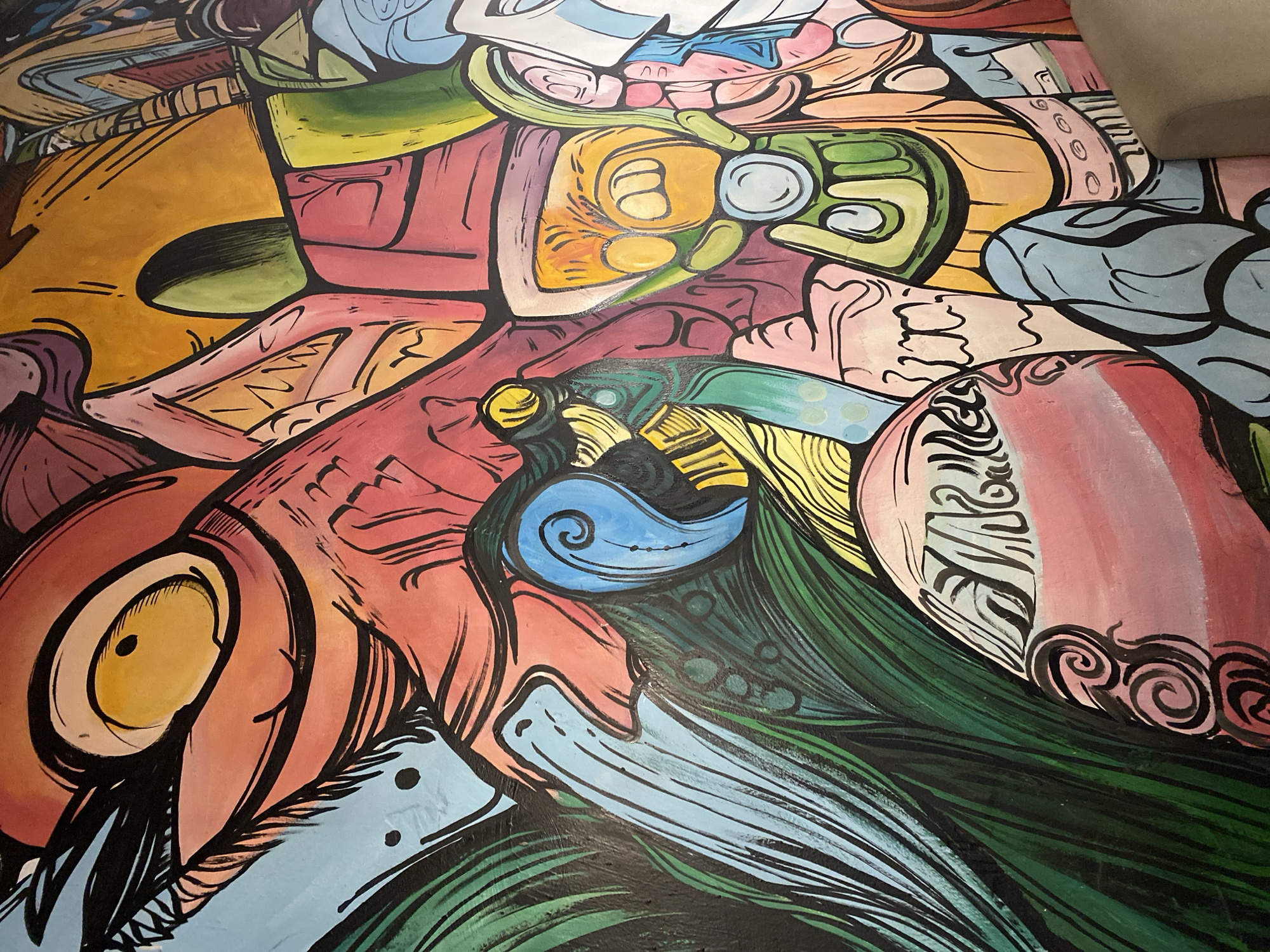 The image depicts a close-up view of a vibrant, abstract mural painted on a wall. The artwork features bold, black outlines and a riot of colors, including shades of red, orange, yellow, green, blue, pink, and purple. The style is characterized by stylized, almost cartoonish figures and shapes, with elements resembling eyes, mouths, and possibly distorted facial features. Some areas have intricate patterns and swirls. The mural appears to be a large-scale piece, likely adorning the exterior or interior of a building.
Based on the available information, this mural is located on the exterior wall of the **Danang Museum of Cham Sculpture** in Đà Nẵng, Vietnam. The museum houses a significant collection of Cham artifacts, and this artistic mural adds a contemporary and colorful element to its facade, likely intended to attract visitors and showcase local artistic expression. The image does not contain any people, identifiable landmarks within Đà Nẵng beyond the museum's presence, or any explicit narrative actions. The focus is solely on the dynamic and colorful visual of the mural itself.