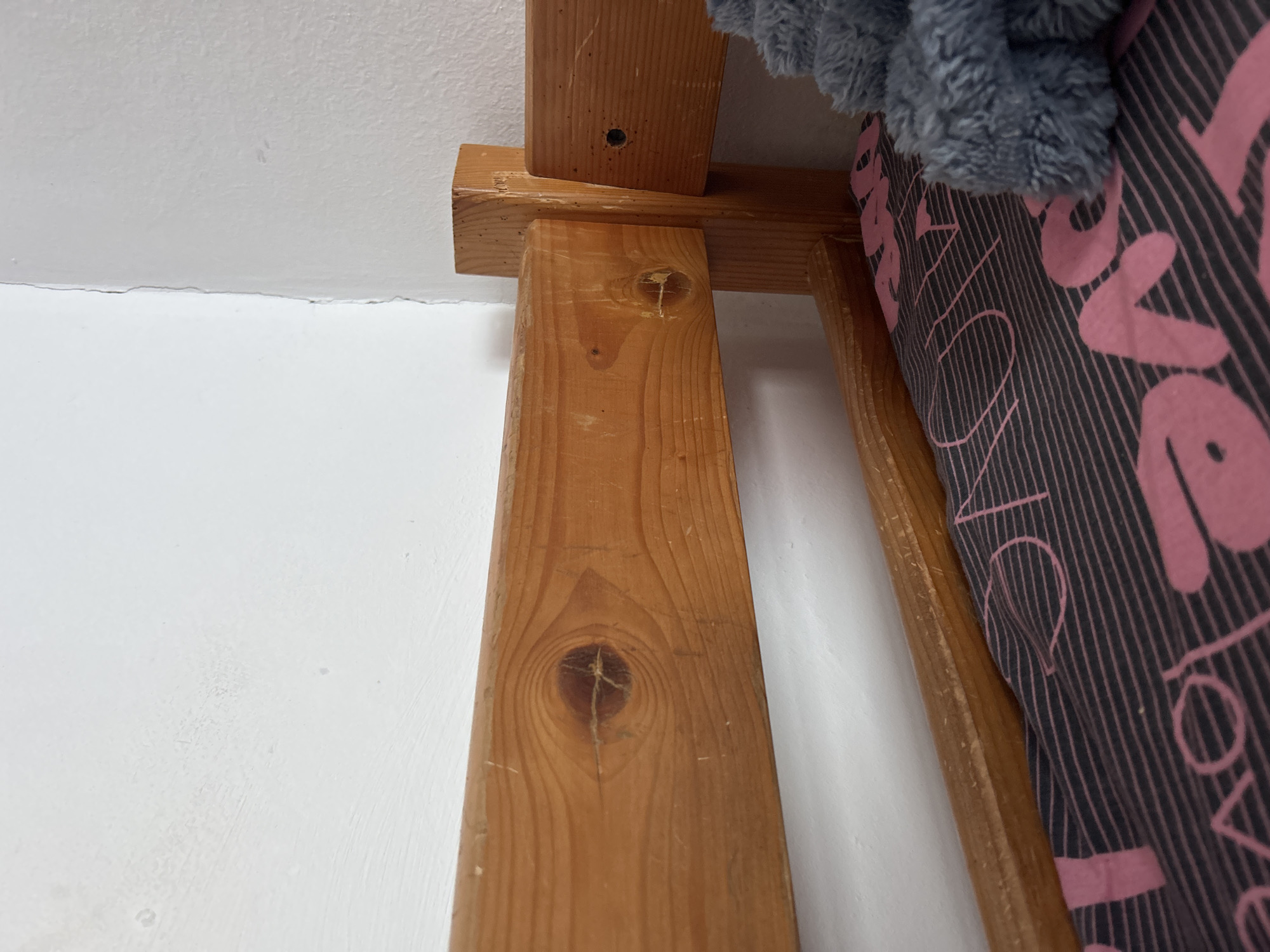 The image shows a close-up of a wooden structure attached to a white wall, likely indoors. The wood has visible knots and grains. There's a gray plush object and a striped fabric with the word "LOVE" printed on it. The location in Sofia, Bulgaria is not evident from the image.
