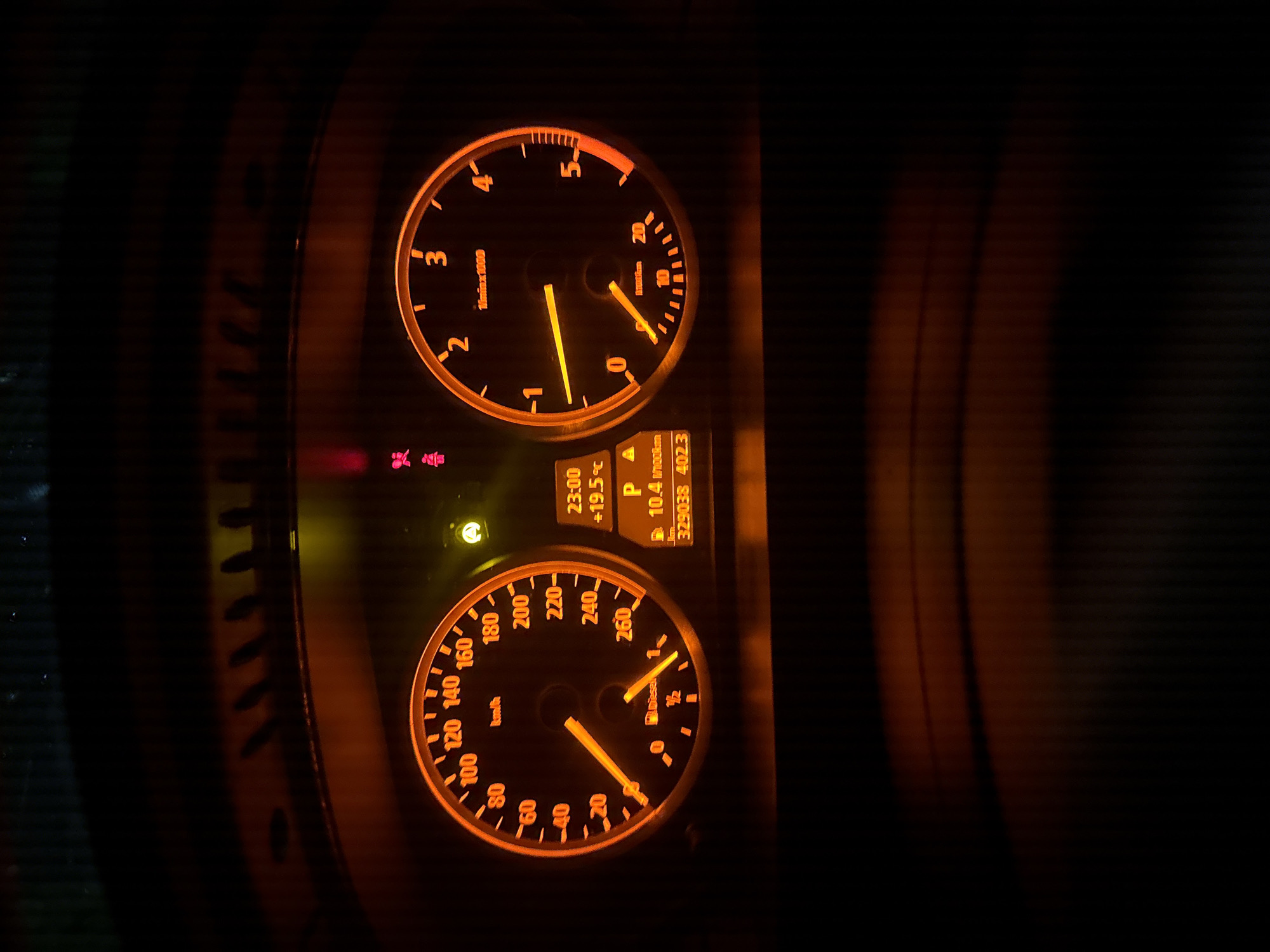 The image shows a car's instrument panel illuminated in a dark environment. The panel includes a tachometer displaying a value between 0 and 1, and a speedometer showing a reading around 20 km/h. An information display indicates the time as 23:00, the temperature as +19.5°C, and the odometer reading as 329038 with a trip meter reading of 402.3. Gear selection is marked as "P." The image provides no data on Stara Zagora, Bulgaria.