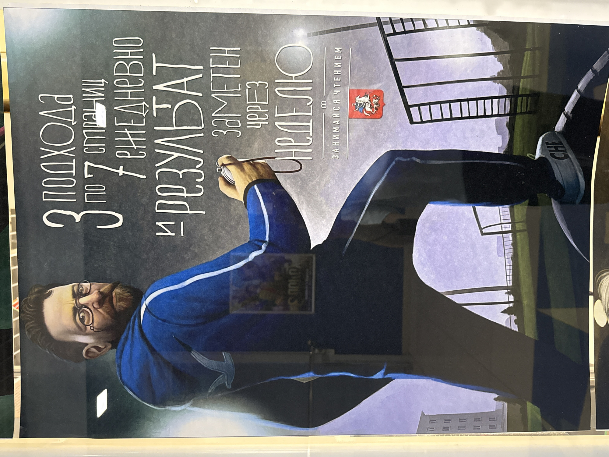 The image is a poster featuring a man in a blue tracksuit with white stripes. He has a beard, glasses, and a stopwatch in his hand. Text on the poster reads "3 ПОДХОДА ПО 7 СТРАНИЦ ПО 7 ЕЖЕДНЕВНО И РЕЗУЛЬТАТ ЗАМЕТЕН ЧЕРЕЗ НЕДЕЛЮ. ЗАНИМАЙСЯ ЧТЕНИЕМ" which translates to "3 APPROACHES OF 7 PAGES EACH, DAILY, AND THE RESULT IS NOTICEABLE IN A WEEK. READ." The poster has a dark, textured background and a coat of arms with a knight on horseback at the bottom. The man is positioned on the left side of the poster, and the text is on the right. The background depicts an outdoor scene with a building, trees, and a sports field with a ladder-like structure. There is no discernible connection to the city of Votkinsk, Russia, in the image itself.