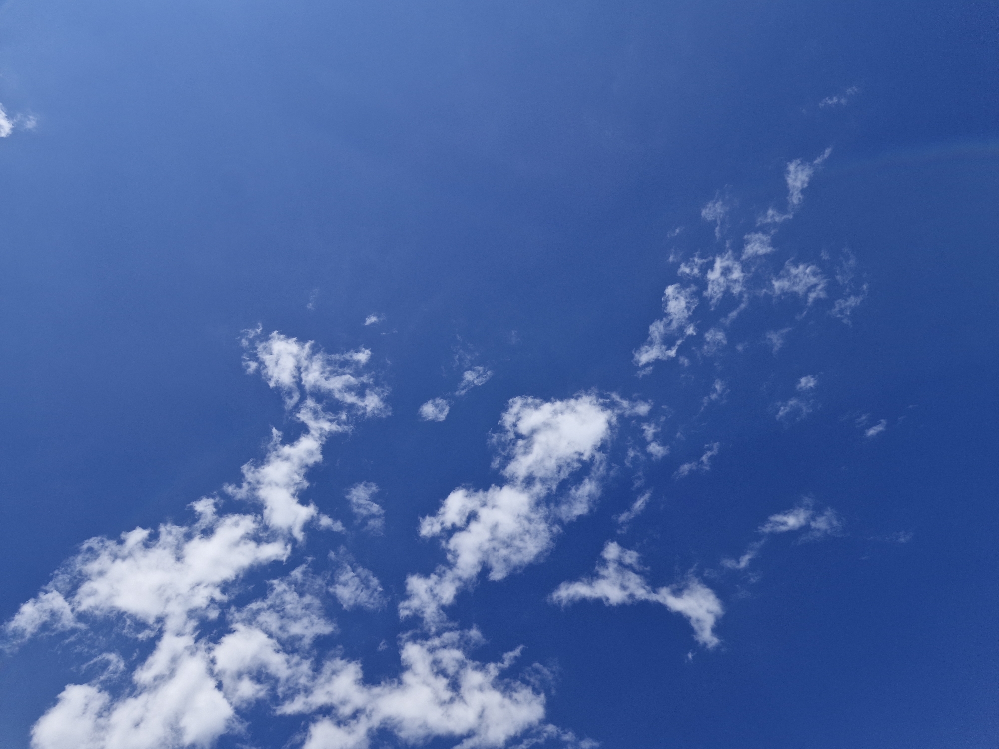 This is a photograph of a blue sky with scattered white clouds. The clouds are wispy and appear to be thin, indicating a clear day. The sky is a deep, vibrant blue, suggesting it is daytime. There is no indication of any structures, people, or specific geographic features in the image. The image appears to be a general shot of the sky and clouds, devoid of any contextual information that would tie it to the city of Bulan-Segettu, Kyrgyzstan, or any other specific location.