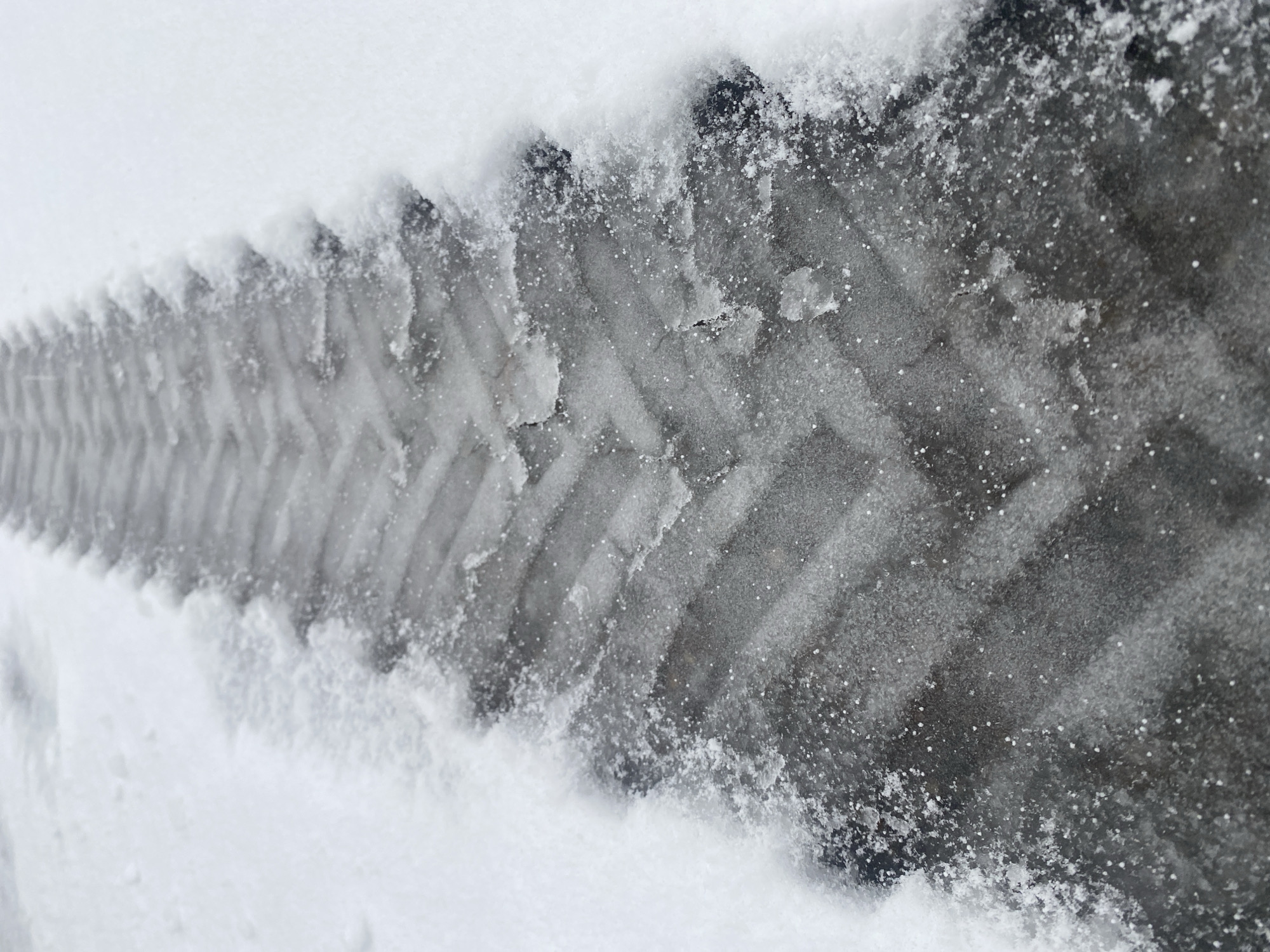 A single tire track is visible in the snow. The track appears fresh, with clean, sharp edges. The surrounding snow is undisturbed except for the tire track. The location is Прикамский, Russia.