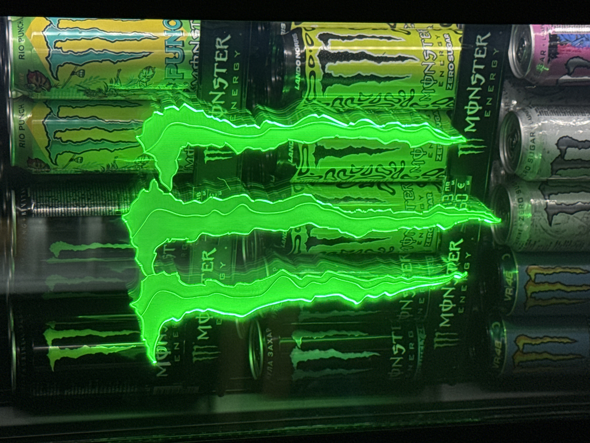 The image shows a shelf of Monster energy drinks in a refrigerated display case. The drinks include various flavors like Rio Punch, Zero Sugar, and Lando Norris. The display case has a green neon Monster logo. The text "ПУЛА ЗАХАР" on a can suggests the image was taken in a location that uses the Cyrillic alphabet, and "NB 13.60 €" indicates a price, possibly from a shop in Veliko Tarnovo, Bulgaria.