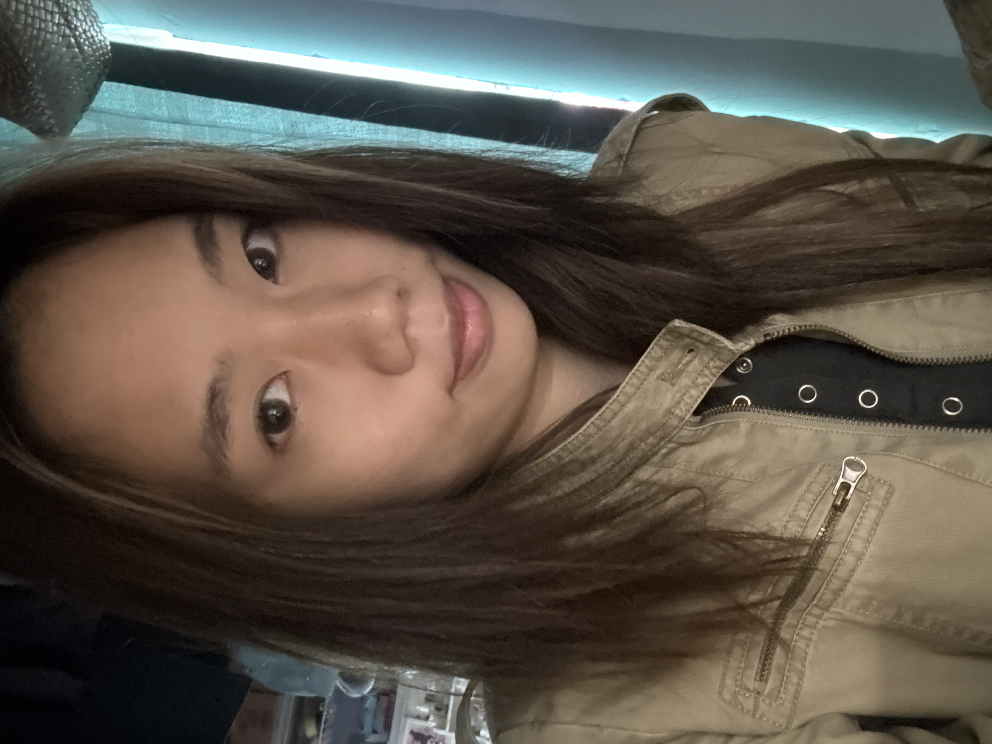 A person with long, brown hair is wearing a tan jacket over a black shirt with metal grommets. The photo appears to have been taken indoors under artificial light. There is no evidence to support the image being in the city of Nan'an District, China.