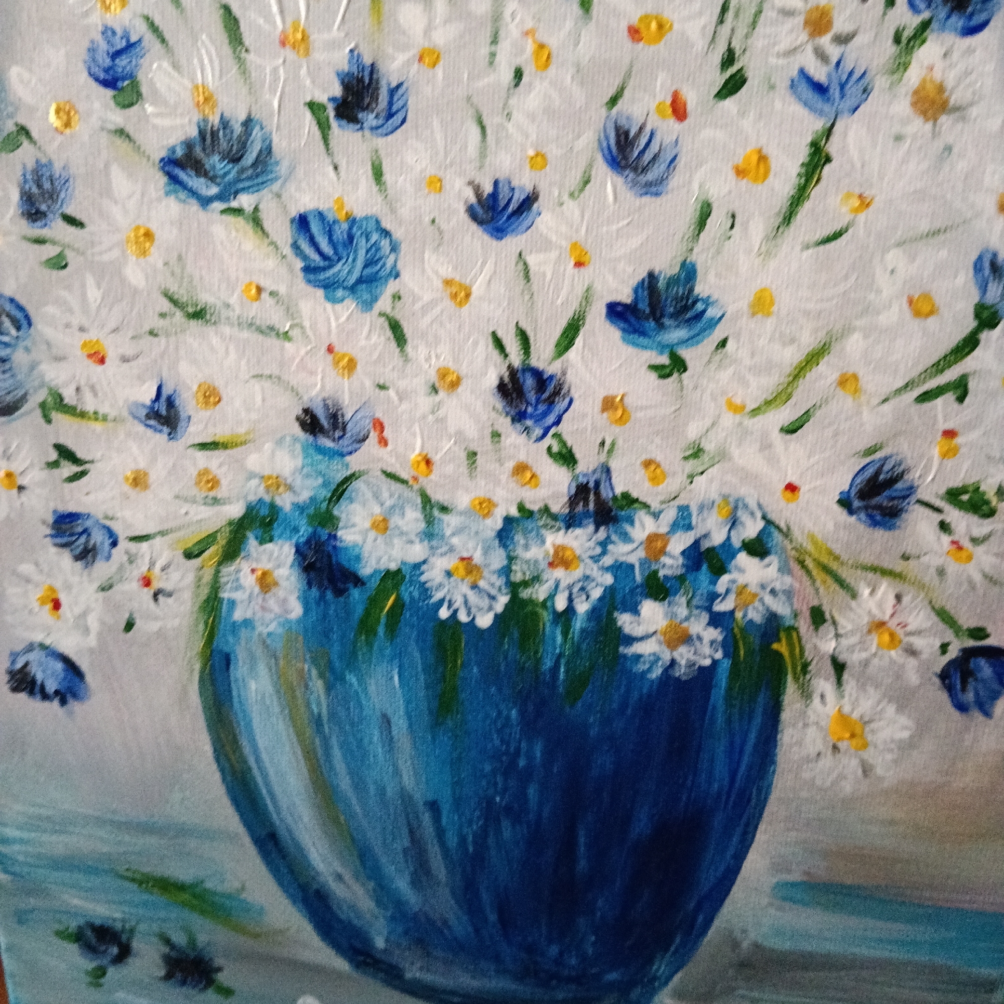 This is an oil painting on canvas, depicting a bouquet of white and blue wildflowers with yellow centers, arranged in a blue vase. The background is a light, textured white, suggesting a wall or fabric. The overall style is impressionistic, with visible brushstrokes. The painting does not show any recognizable landmarks or elements that would place it specifically in the city of Oliva, Spain.