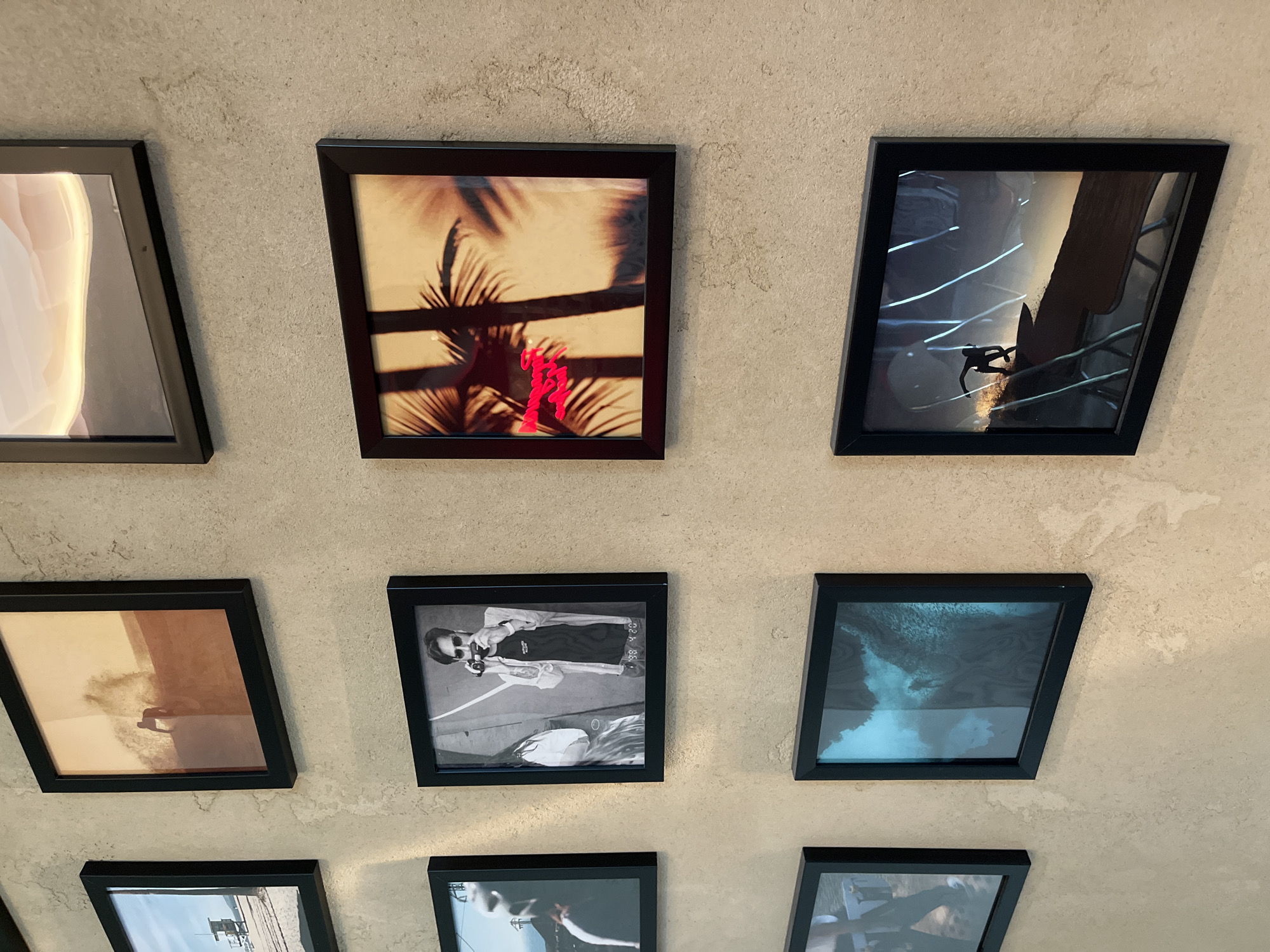 This image shows a wall decorated with framed photographs. The photographs appear to be of varying subjects, including landscapes, people, and abstract imagery. The wall itself has a textured, concrete-like finish. The scene is indoors and well-lit, suggesting it could be a home, gallery, or commercial space. The specific location in the city of Kazan, Russia cannot be determined from the image alone. There are no people visible in the immediate scene interacting with the photographs.