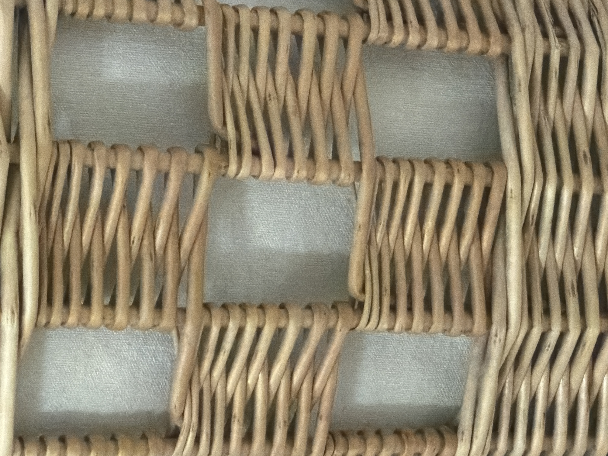 The image shows a close-up of a woven basket. The basket is made of light-colored wicker material and has a checkered pattern. The weave is tight and appears to be in good condition. The background is a textured, light-colored fabric, possibly a wall or upholstery. There are no people or any identifiable landmarks present that would indicate a specific location in Khmelnytskyi, Ukraine.