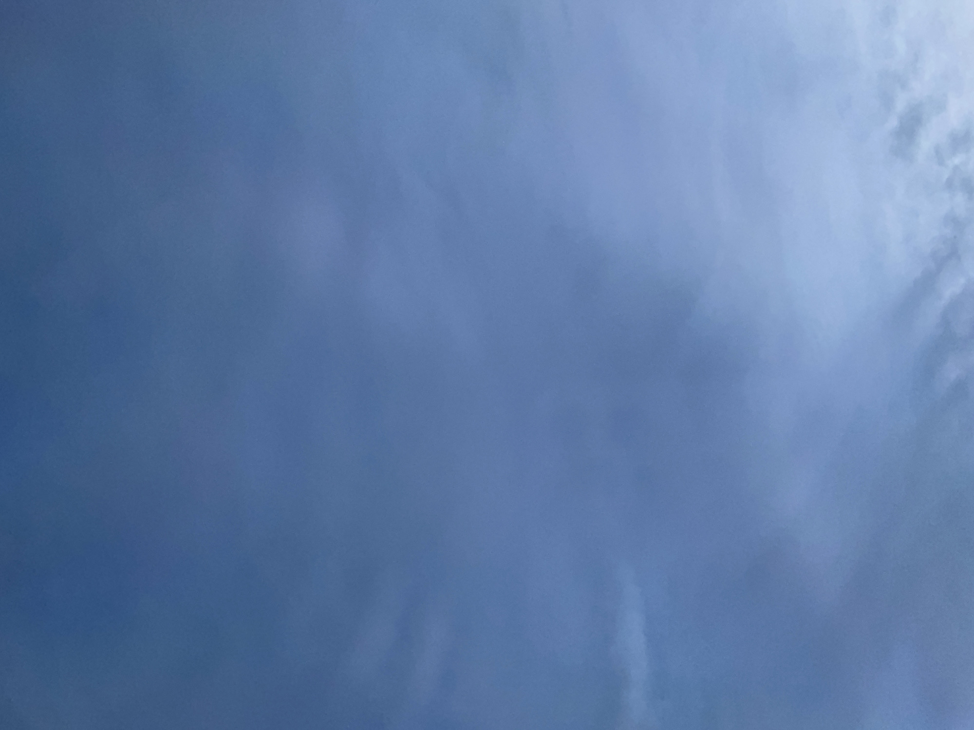 The image shows a slightly hazy, overcast sky with a muted blue hue. Some wispy clouds are visible, especially towards the bottom of the frame where they are darker and more defined. The overall impression is of a cool, perhaps twilight, atmosphere. There are no discernible objects, people, or structures in the image, nor any indication of a specific location within a city.