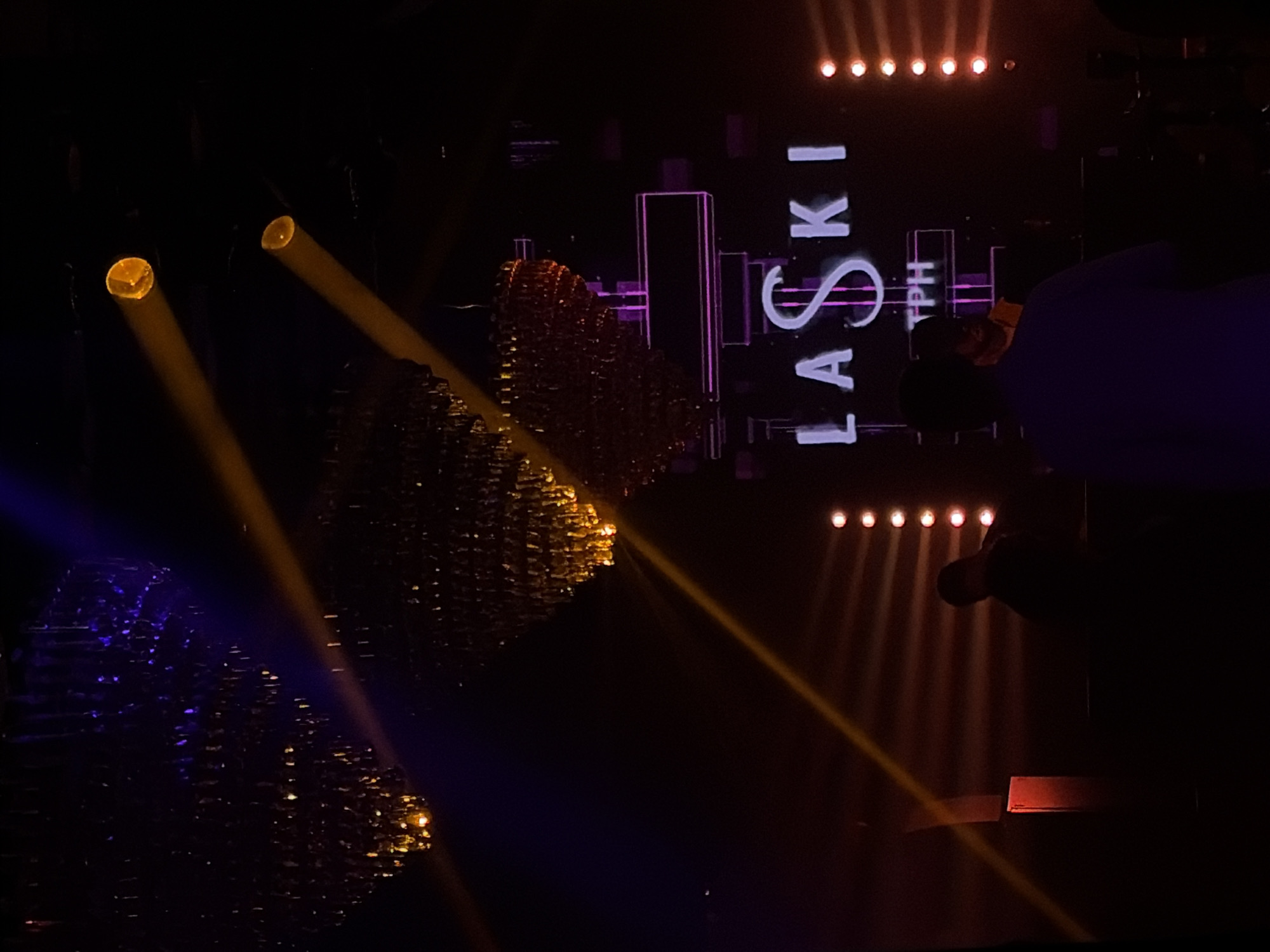 The image shows a stage setup at what appears to be a performance venue in Moscow, Russia. The text "LASKI TPH" is visible, possibly related to the event or performers. There are stage lights casting illumination, and a person is visible in the background. Objects resembling decorative elements or reflective surfaces are present on the left side of the stage. The stage is darkened, lit primarily by stage lighting.