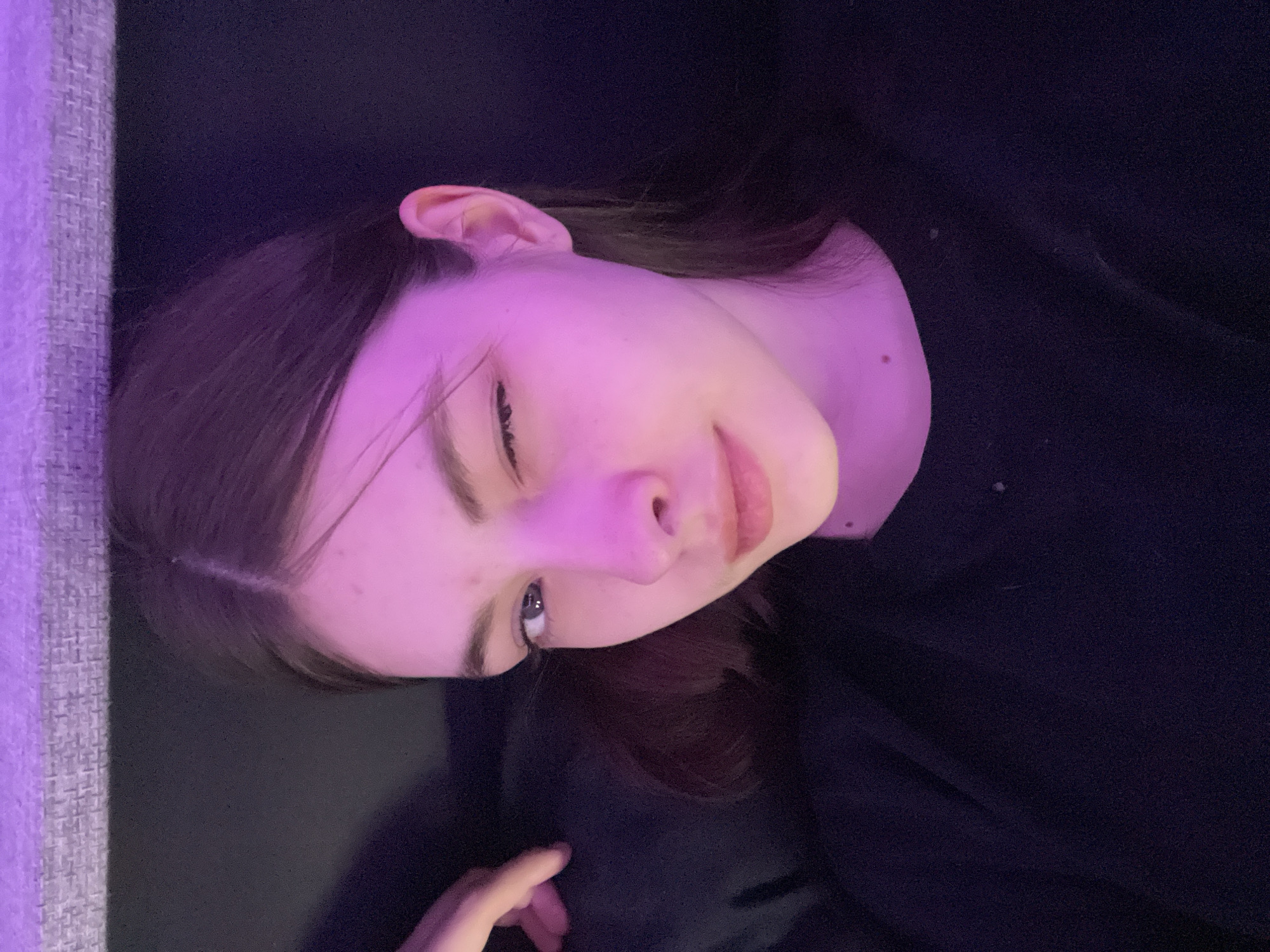A young person with fair skin, dark hair, and a neutral expression is lying down. They are wearing a dark top. The background is dark and appears to be a piece of furniture or bedding. There are no visible landmarks to indicate the city of Saint Petersburg, Russia.