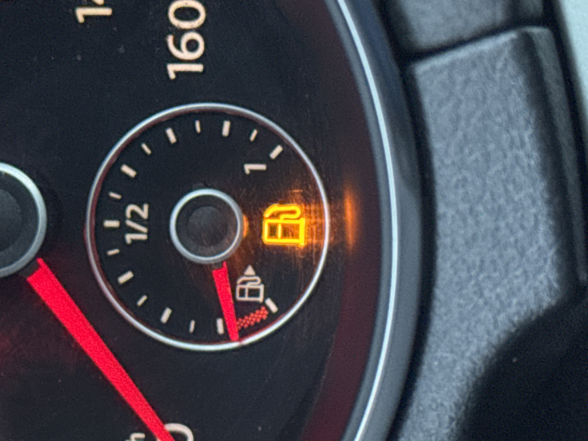 The image shows a portion of a car's dashboard. The fuel gauge indicator needle is pointing to the "E" indicating the fuel tank is empty. The low fuel warning light, shaped like a gas pump, is illuminated. The speedometer dial shows the numbers "160" suggesting it measures speed in kilometers per hour. The location is not possible to determine from this image.